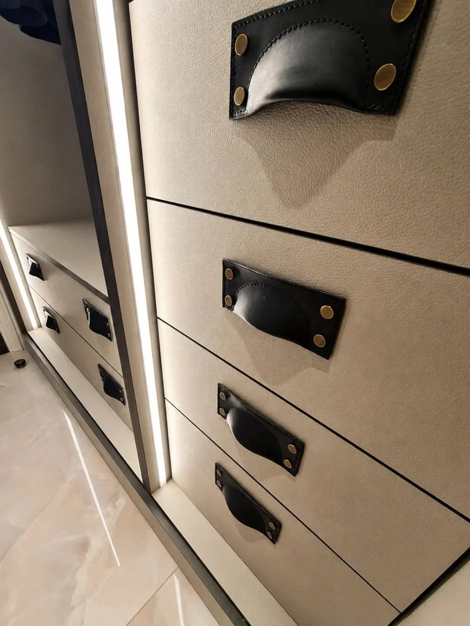 Close-up of bespoke leather-effect drawer fronts with custom handles and integrated lighting inside a luxury walk-in closet.