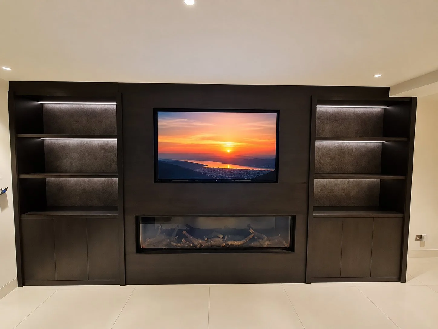 Luxury media unit featuring a recessed television, integrated fireplace and symmetrical LED-lit display shelving with fitted storage.