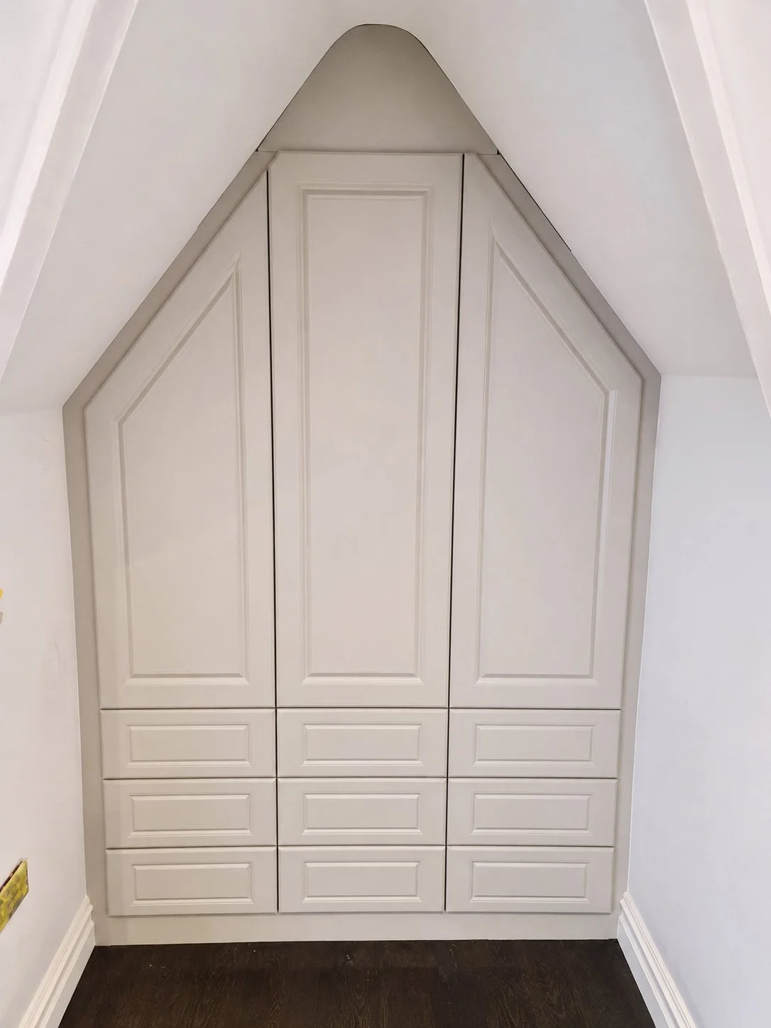 A fitted alcove wardrobe with shaker-style doors, bespoke cabinetry and precision detailing shaped to follow the room's angled ceiling.