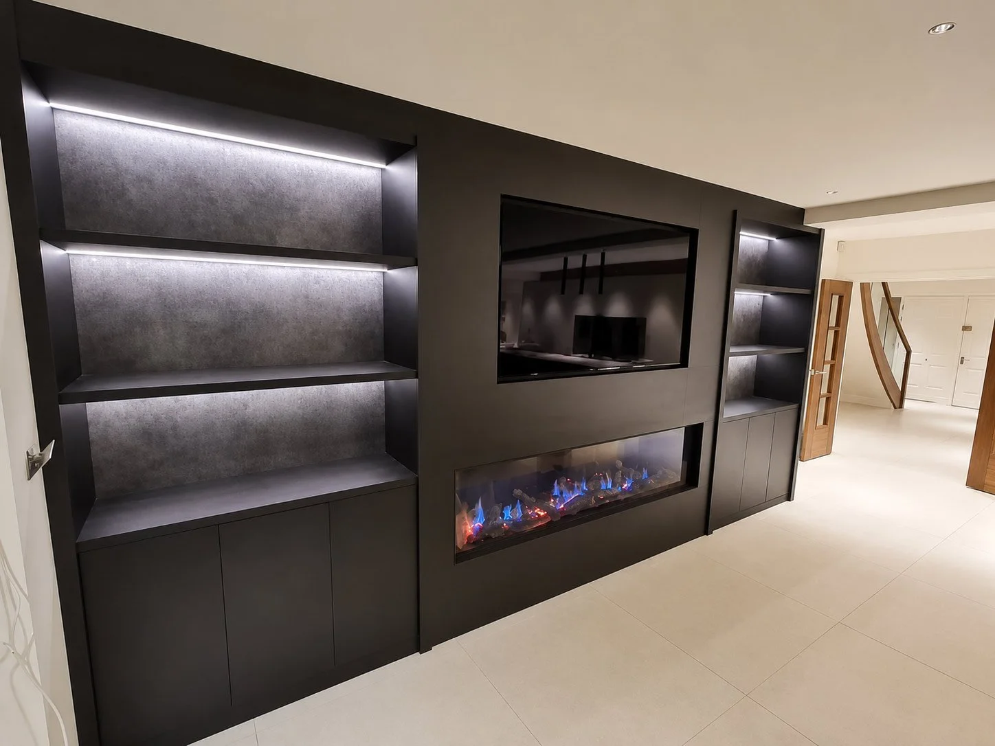 Luxury media unit featuring a recessed television, integrated fireplace and symmetrical LED-lit display shelving with fitted storage.