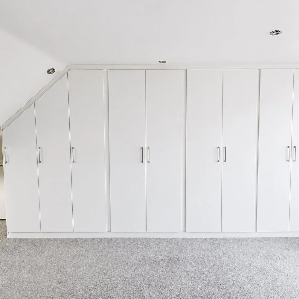 A custom loft wardrobe interior with shelving, hanging rails and fitted compartments designed around an angled ceiling.