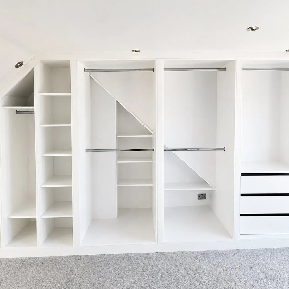 A made-to-measure loft wardrobe with angled cabinetry, open shelving, hanging space and integrated storage designed to maximise a sloping roofline.