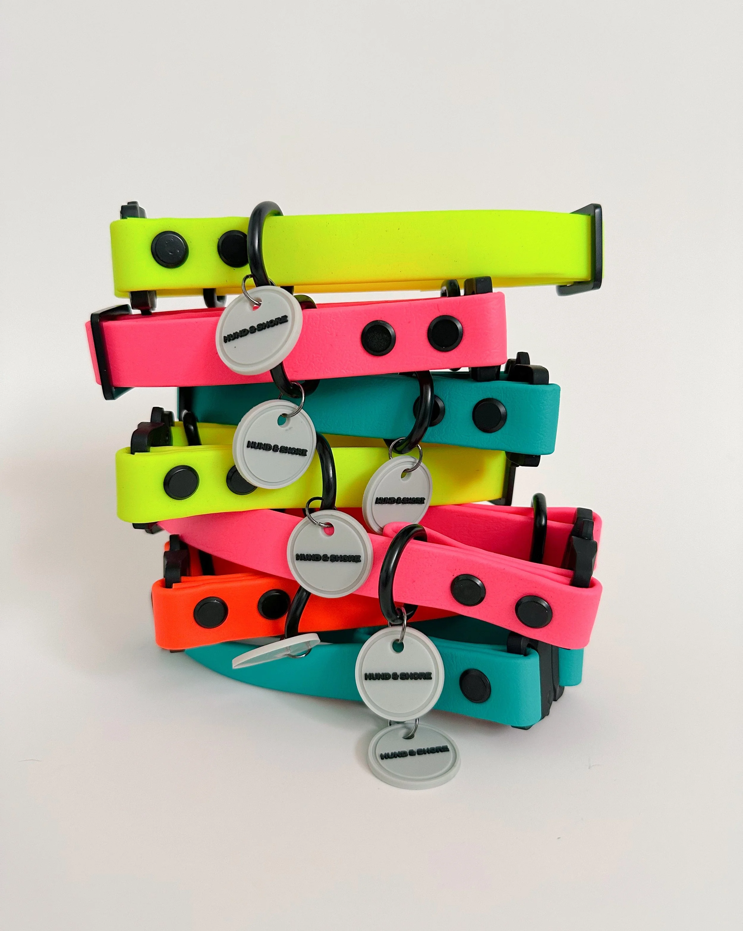 Stacked colorful dog collars with black buckles and tags labeled 'HUND & SHORE' on a white background.