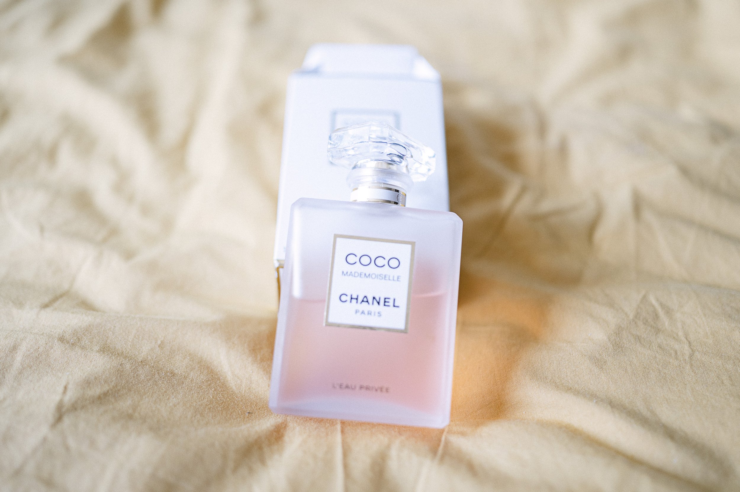Flacon de parfum Chanel Coco Mademoiselle en couleur rose pâle, placé sur une surface en tissu beige
