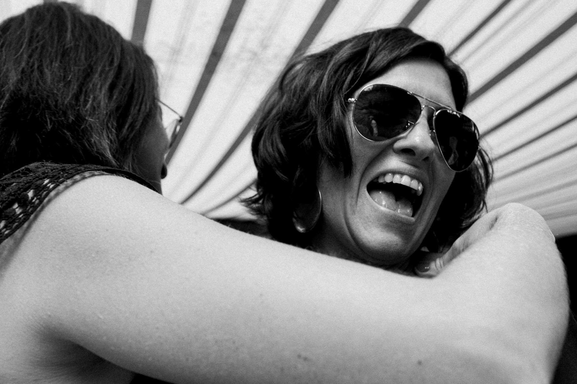 Deux femmes sont en train de s'étreindre et l'une d'elles porte des lunettes de soleil noires, elles semblent rire.