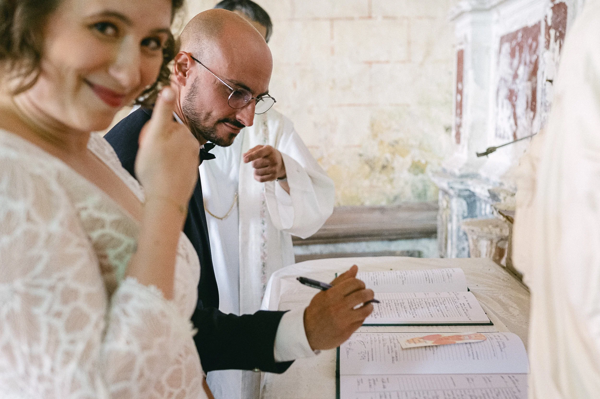 Un couple lors d'une cérémonie de mariage, assis à une table, en train de signer un document officiel.