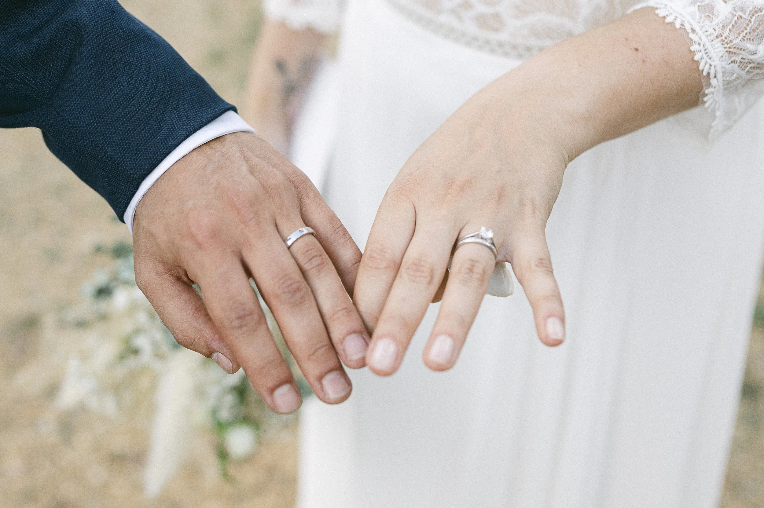 Les mains d'un couple marié, avec les alliances en argent, échangeant un pacte d'engagement ou de mariage lors d'une cérémonie en extérieur.