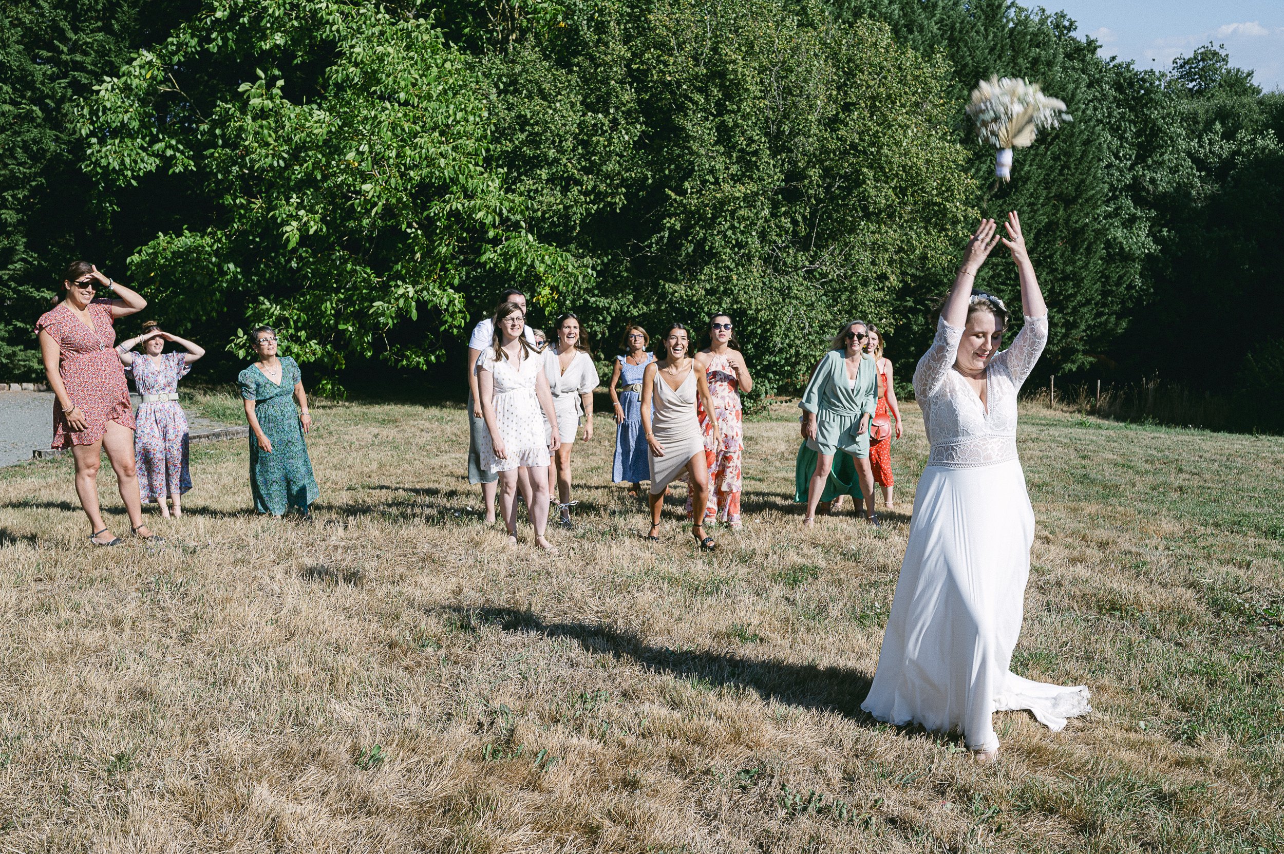 Un groupe de femmes habillées en vêtements d'été apparentent assister à une activité en plein air, avec une femme en robe blanche lançant un objet en l'air, dans un environnement naturel avec des arbres.
