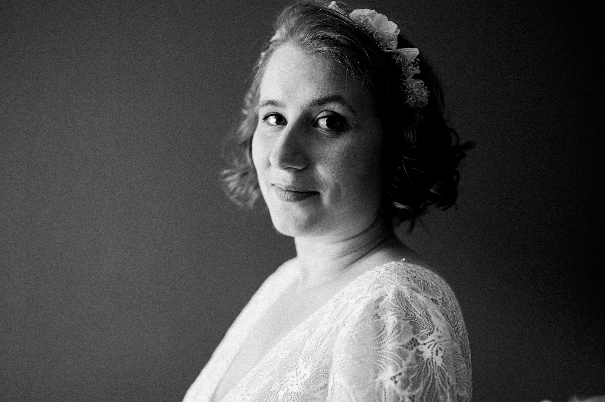 _portrait en noir et blanc d'une femme avec des cheveux courts et ondulés portant une robe en dentelle, elle regarde en direction de l'objectif avec un léger sourire.