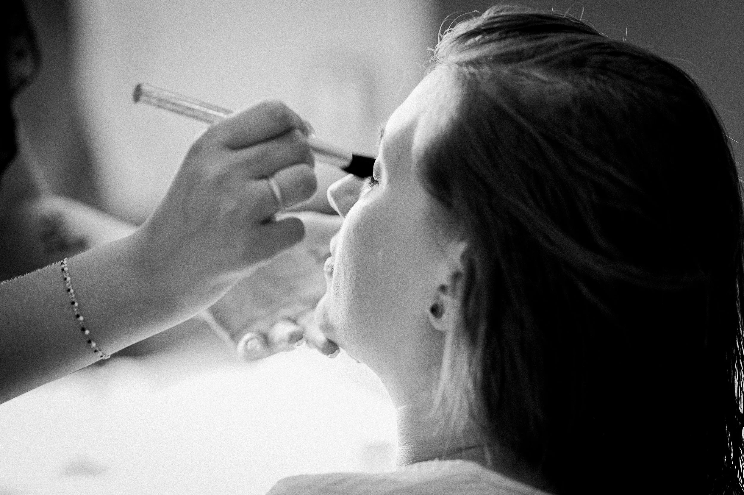 Une femme reçoit un maquillage des yeux par une autre personne, en noir et blanc.