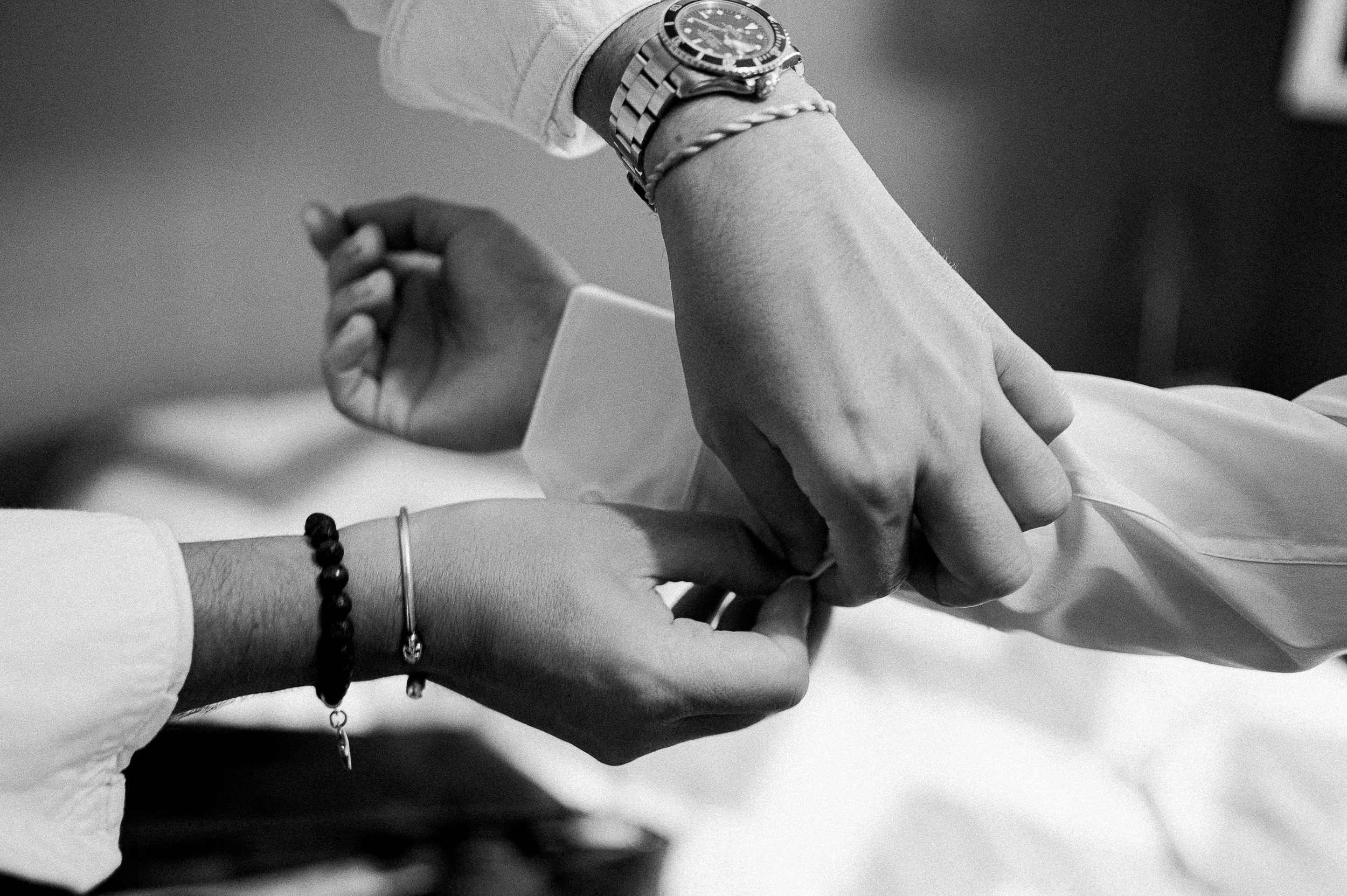 Deux mains qui se tiennent, l'une portant une montre en acier, l'autre un bracelet noir avec perles.