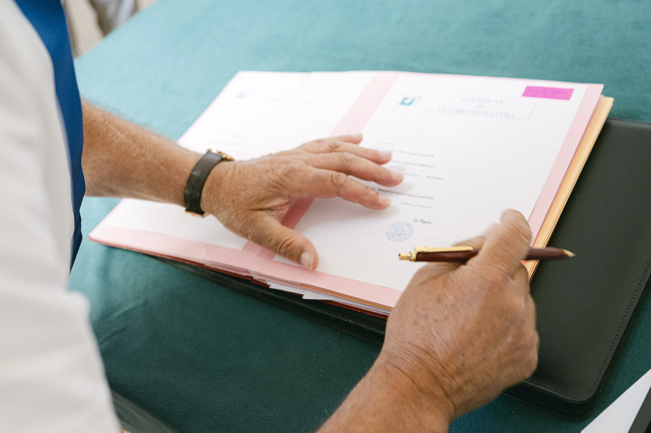 Une personne signe un document officiel sur une table verte.