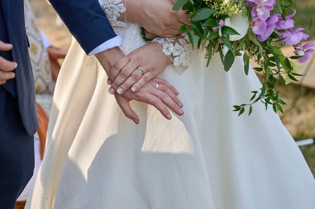 Les mains d'un mariage, avec une bague, tenues de mariage blanches et un bouquet de fleurs.