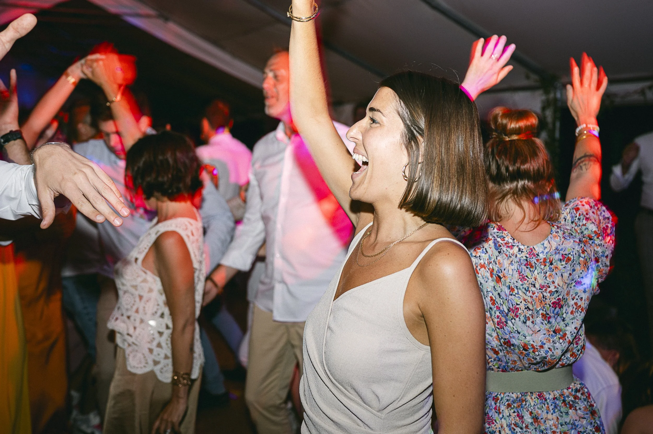 Groupe de personnes dansant et s'amusant lors d'une fête ou d'un événement social, sous un éclairage coloré, avec une femme souriante en premier plan.