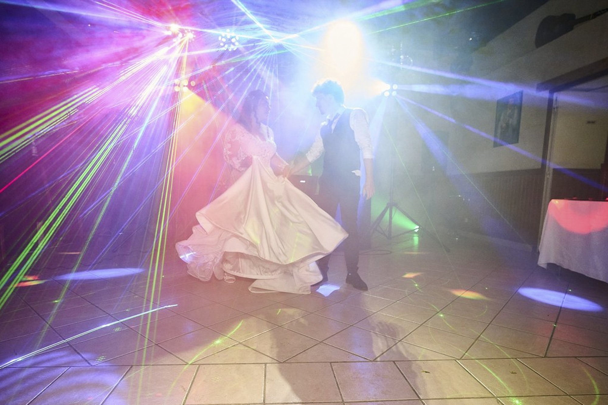 Un couple danse lors d'une réception ou d'une fête avec des effets de lumières colorées et des lasers.