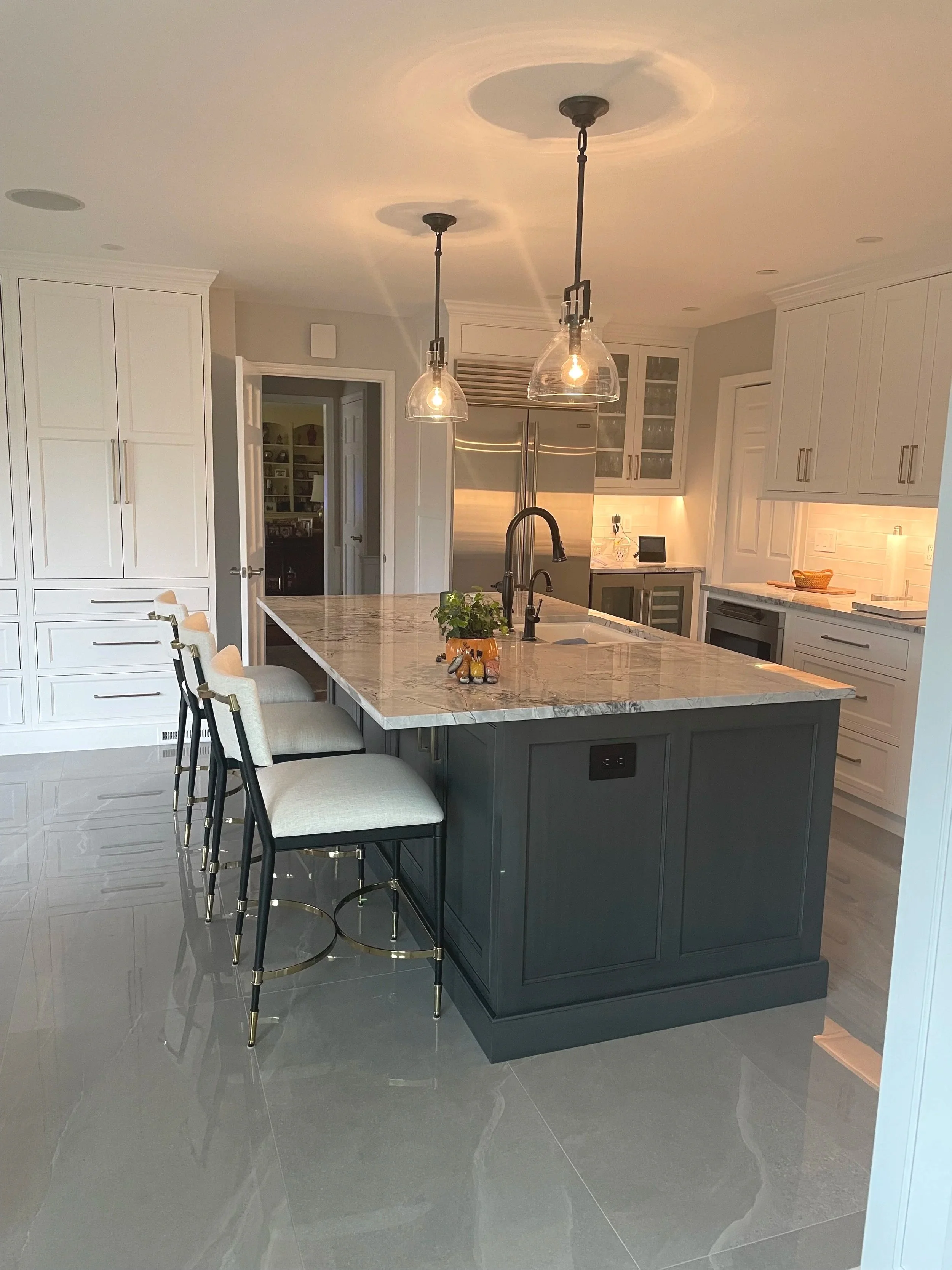 Modern kitchen with gray cabinetry, a marble island, beige chairs, stainless steel refrigerator, pendant lights, and a tiled floor.