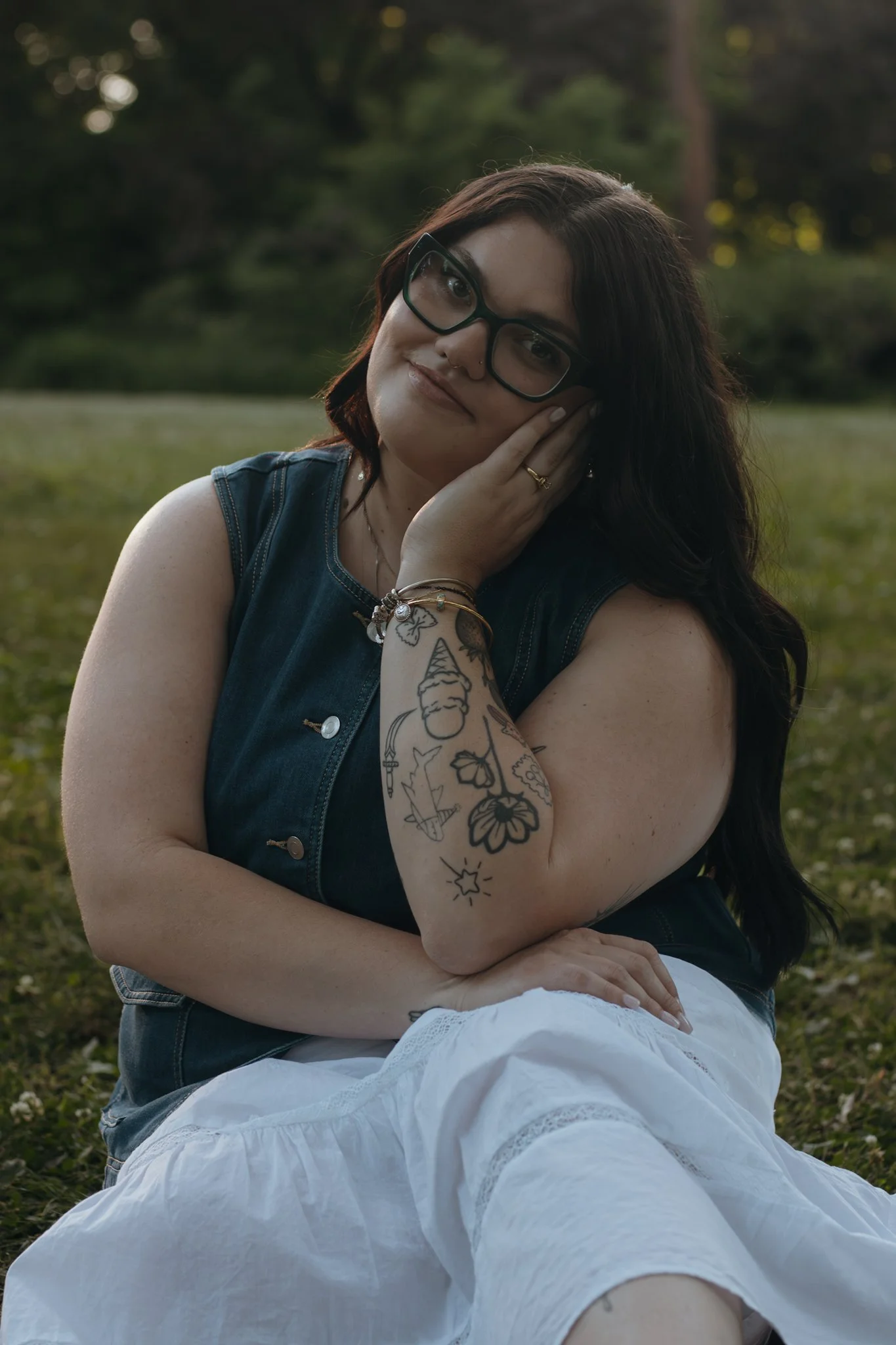 Smiling woman with dark hair and glasses, wearing a black lace top, against a plain gray background.