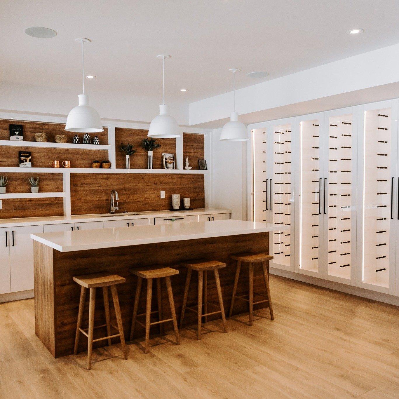 We love designing basements ready for entertaining!
This white kitchen with wood accents feels warm and elegant and the built-in wine cellar brings the design together while giving the home owner a place to showcase their wine collection.🍾

Architec