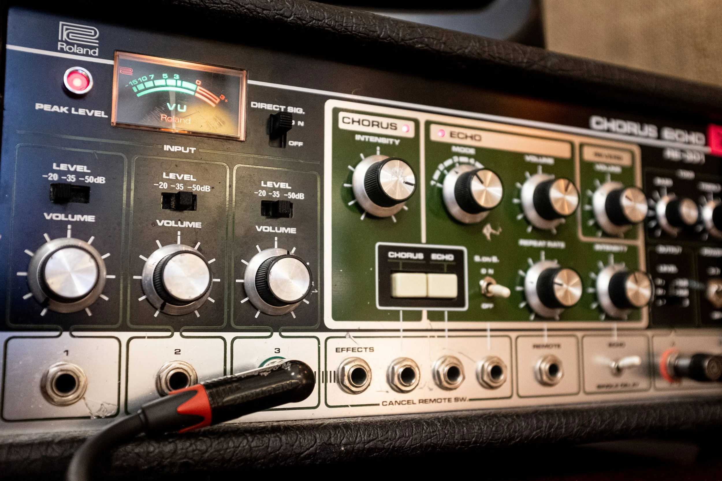 Et lydkonsoll med justeringsknapper og etiketter, inkludert en VU-meter og kabler tilkoblet til inngangene.