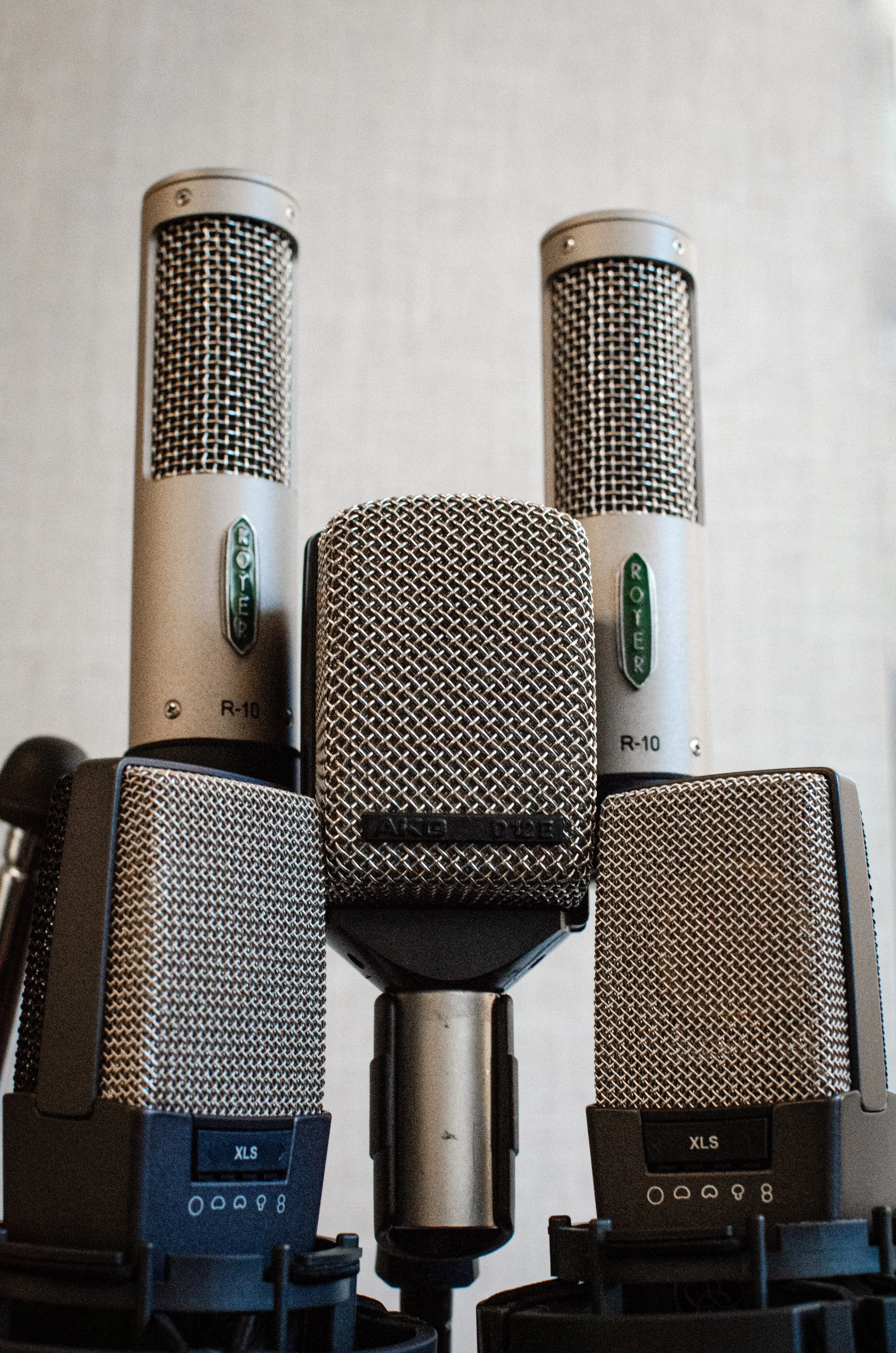 Fem mikrofoner av forskjellige modeller og merker plassert på et stativ mot en lysegrå vegg.