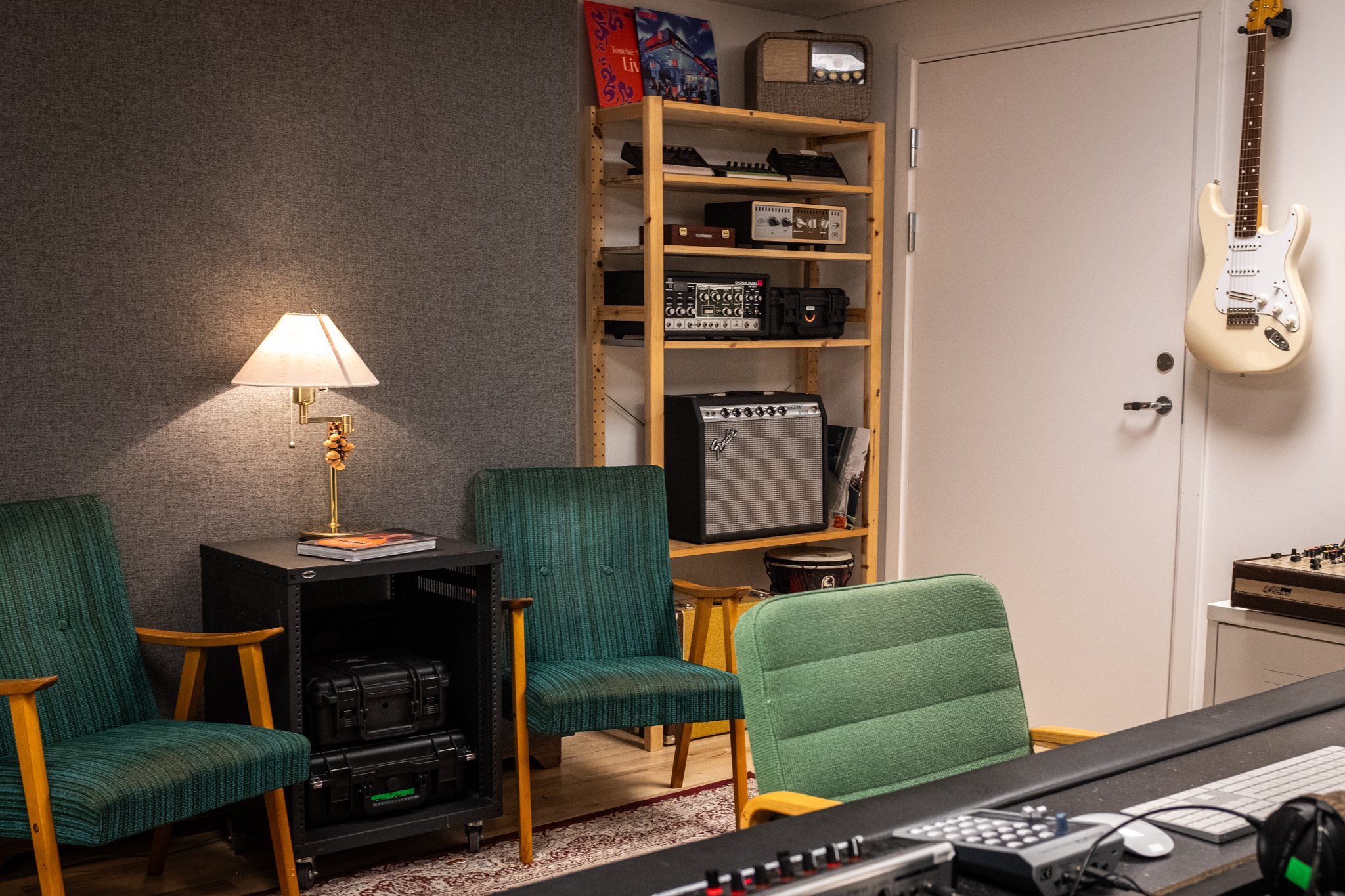 Rom med musikutstyr, including gitar på veggen, forsterkere, mixer, og møbler med grønne stoler