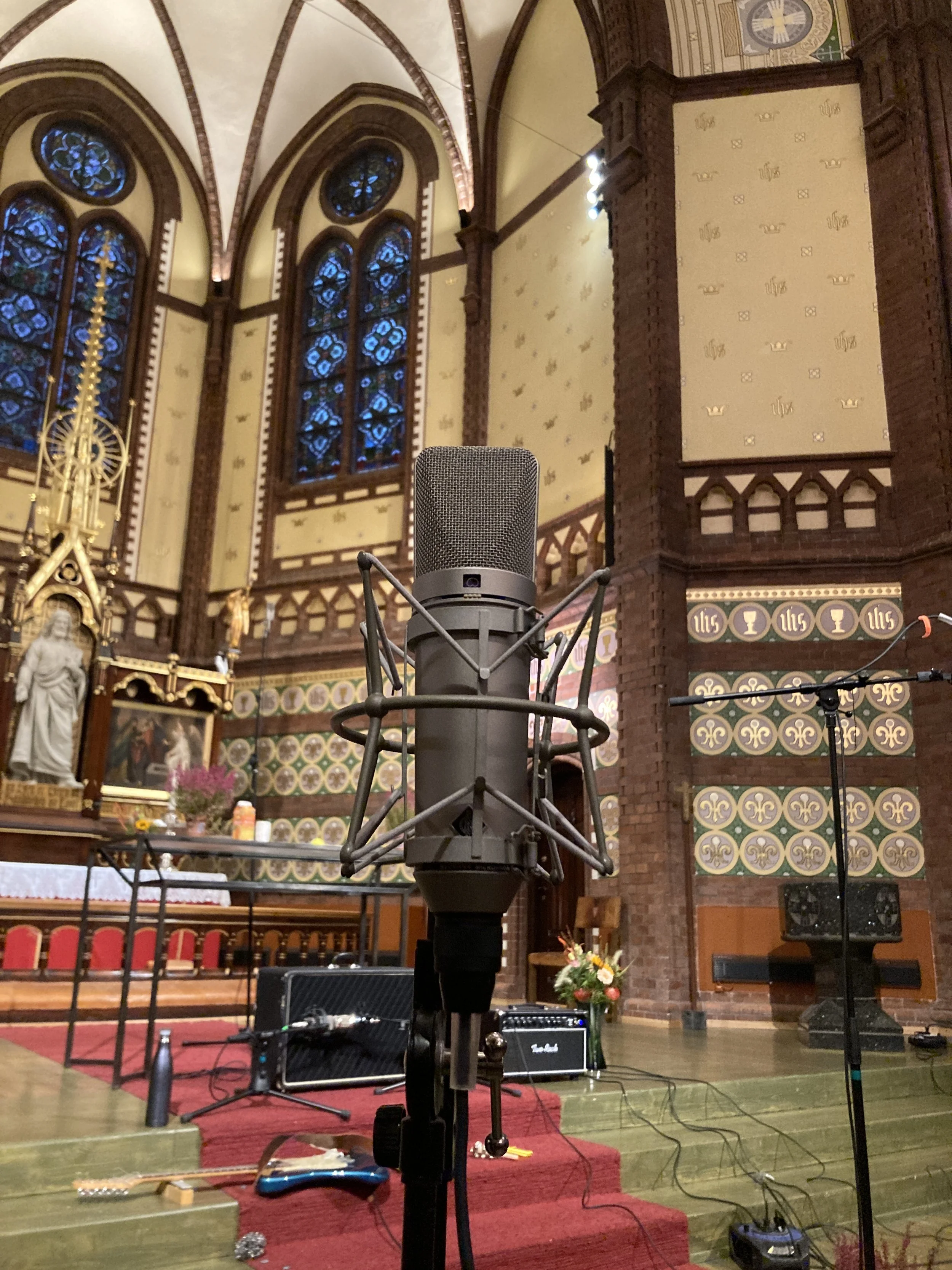 Innendørs scene i en kirke med mikrofon i forgrunnen, musikkutstyr og alter i bakgrunnen.