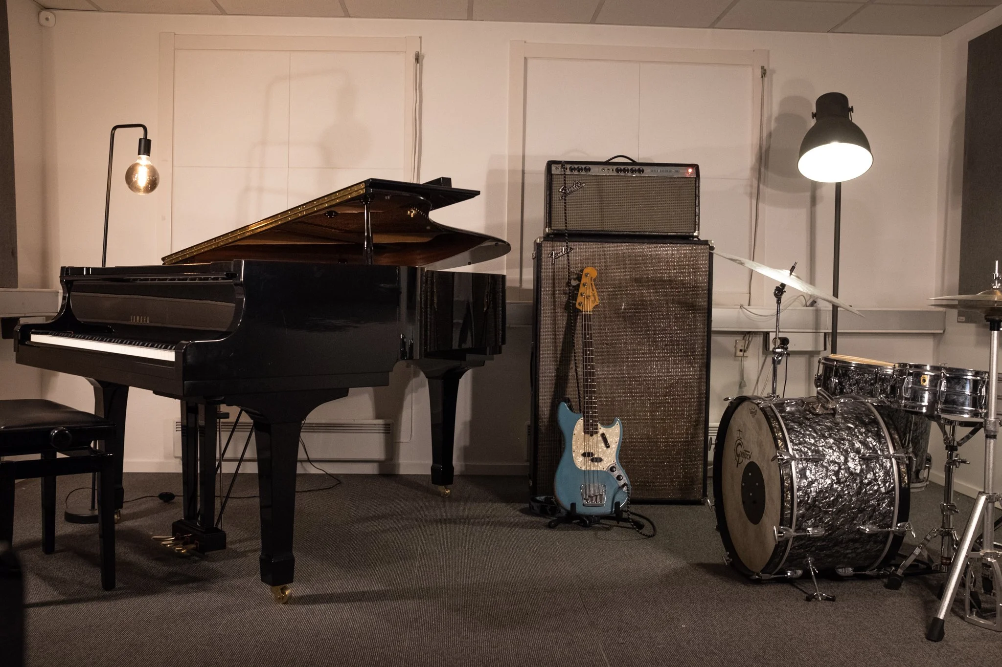 Et musikkompisasjonsrom med piano, elektrisk bass, forsterkere, trommesett og musikkutstyr.