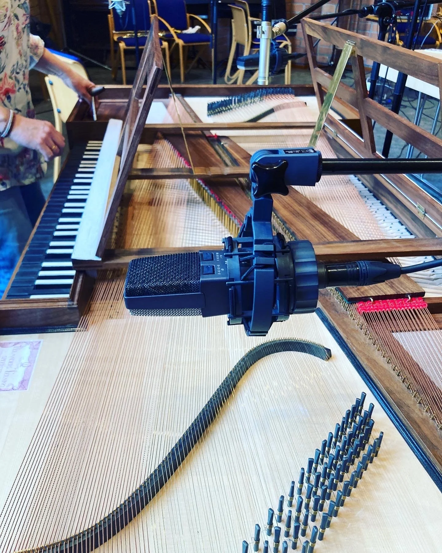 Innvendig bilde av en åpen flygel med mikrofon og opptaksutstyr plassert over strengene, omgitt av stoler og andre musikkinstrumenter.