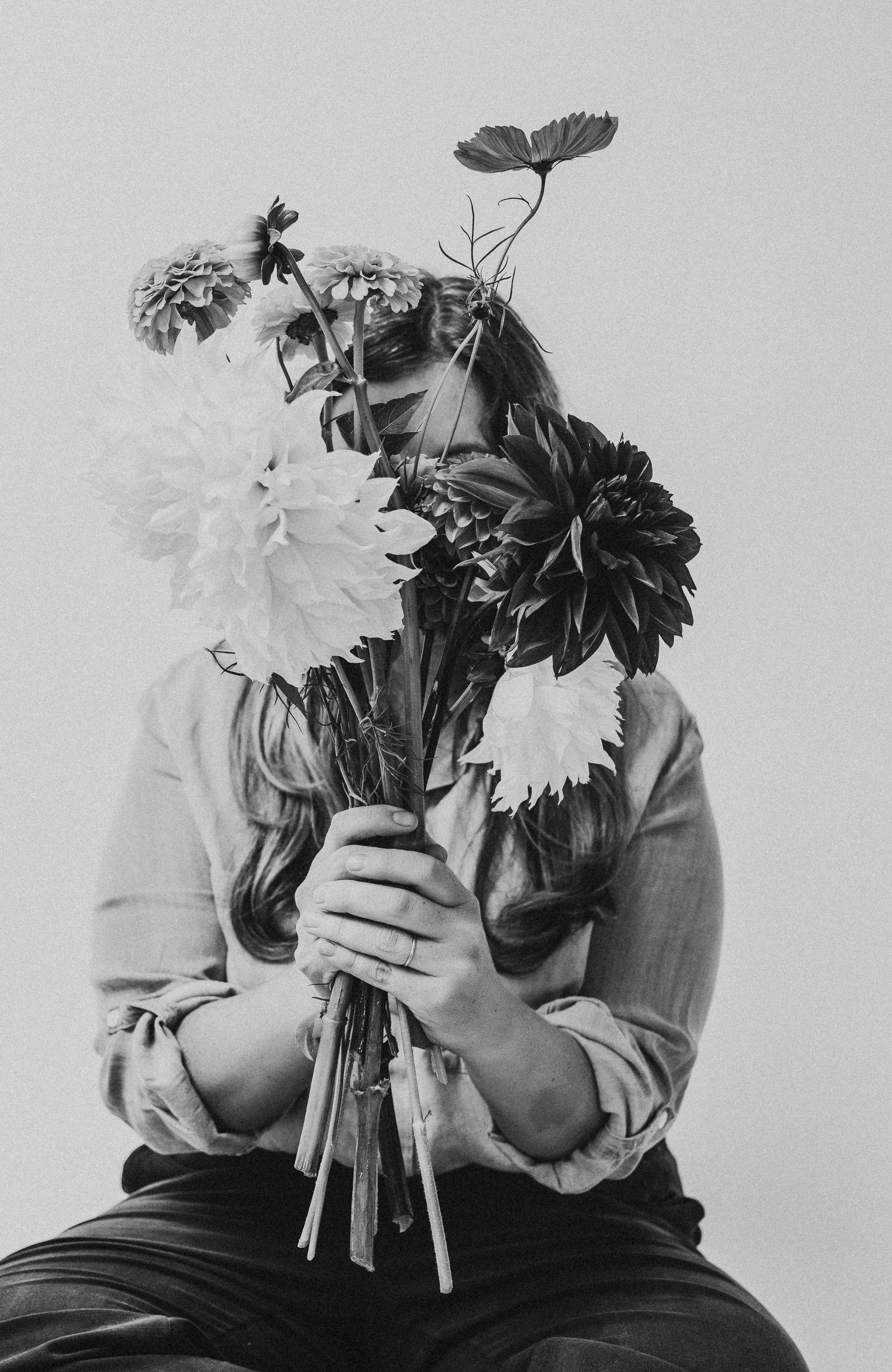 Person holding a bouquet of flowers in front of face, black and white photo.