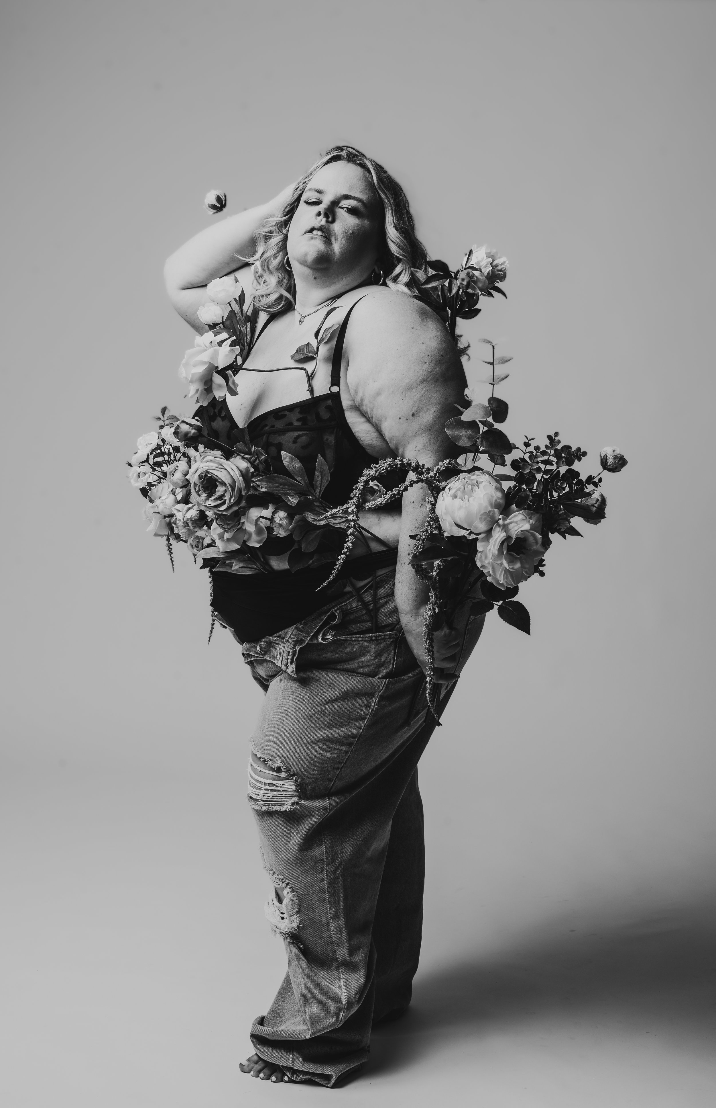 Black and white photo of a person wearing ripped jeans and adorned with flowers.