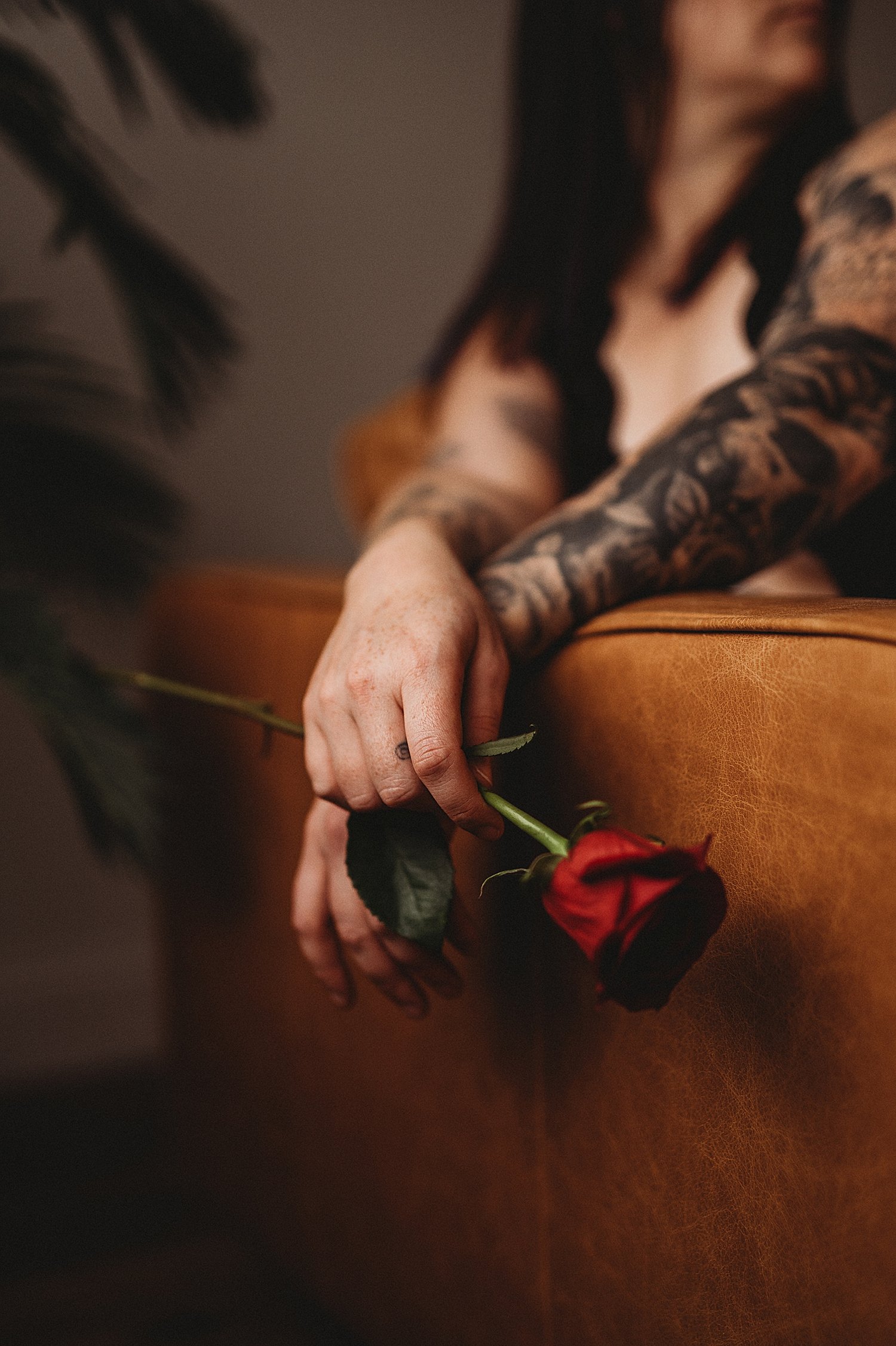  two hands with tattoos over the back of a couch holding a rose by New Hampshire Boudoir Photographer 