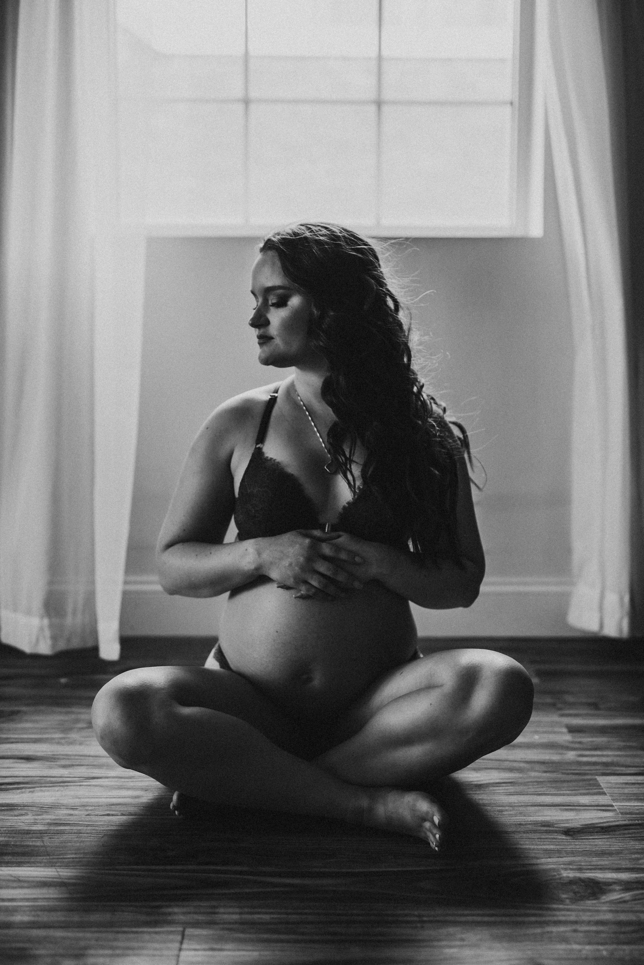 Pregnant woman sitting on the floor with hands on belly, black and white photo