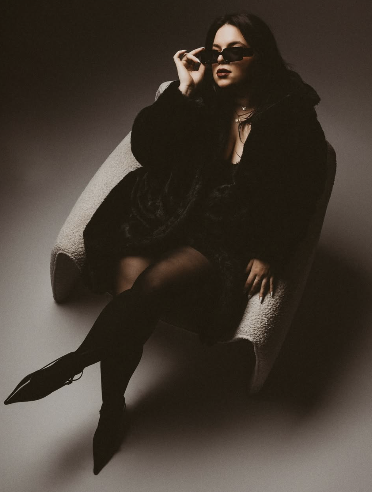 brunette in fur coat and sunglasses in a chair in studio