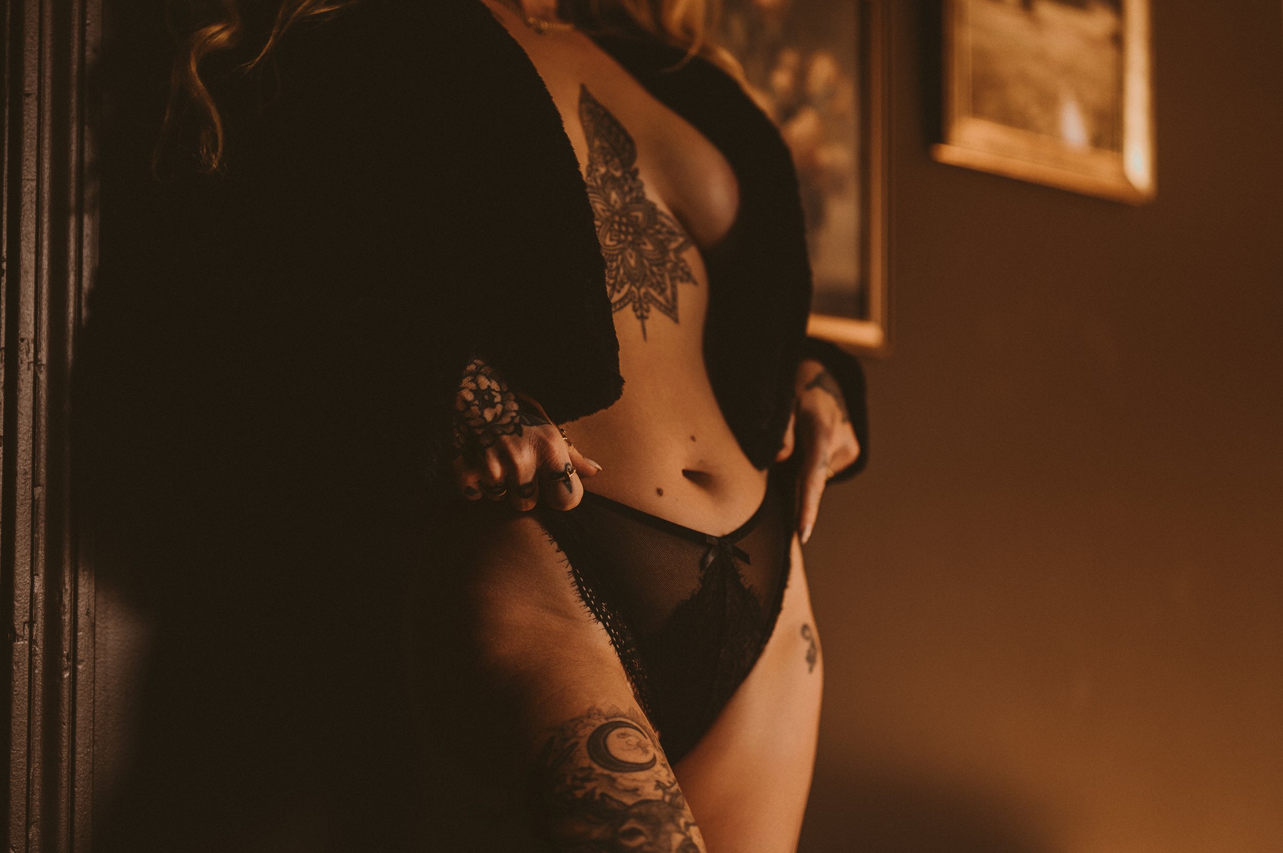 Person wearing black lingerie with tattoos on their body.
