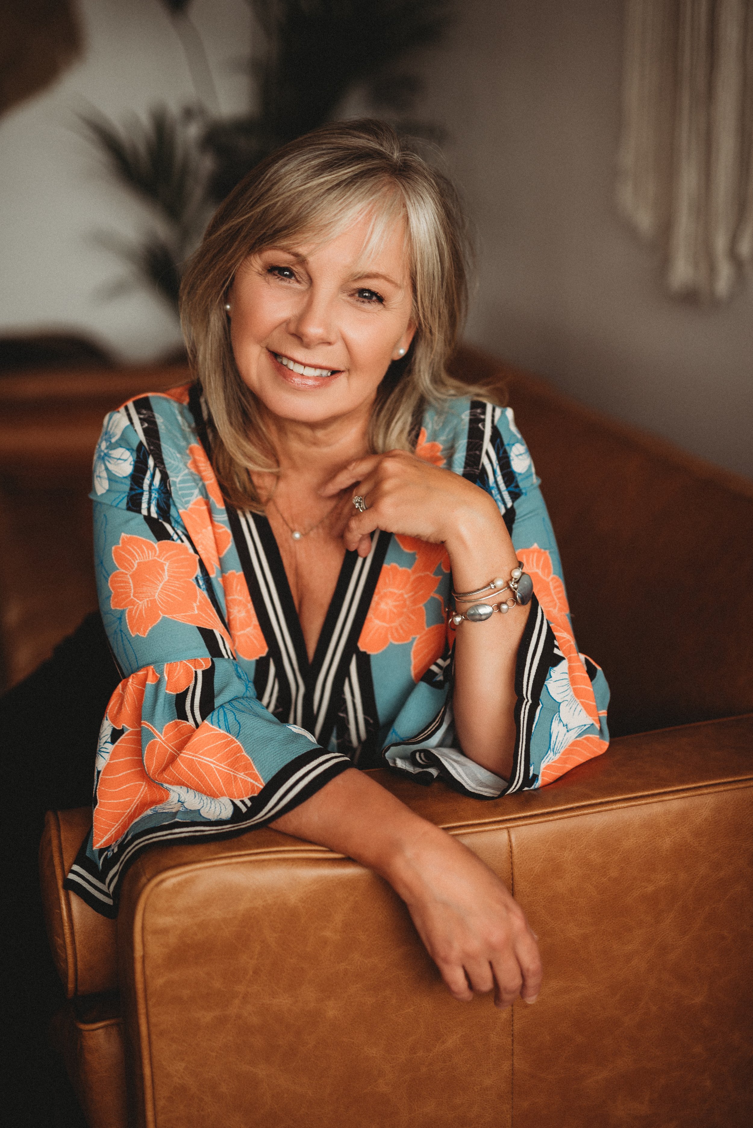 Smiling woman in floral blouse sitting on a leather couch.