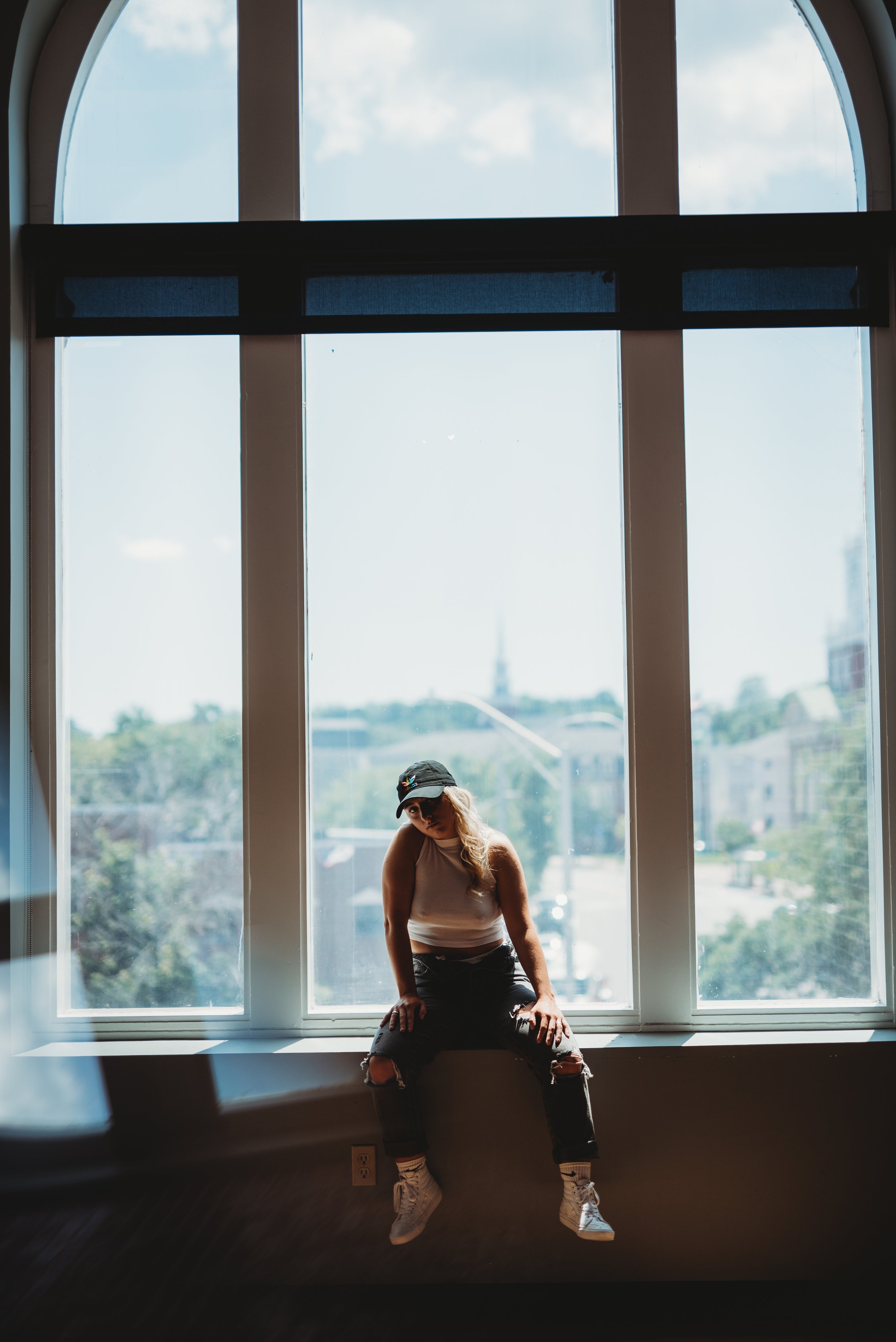 Person sitting on a window ledge with a cityscape view.