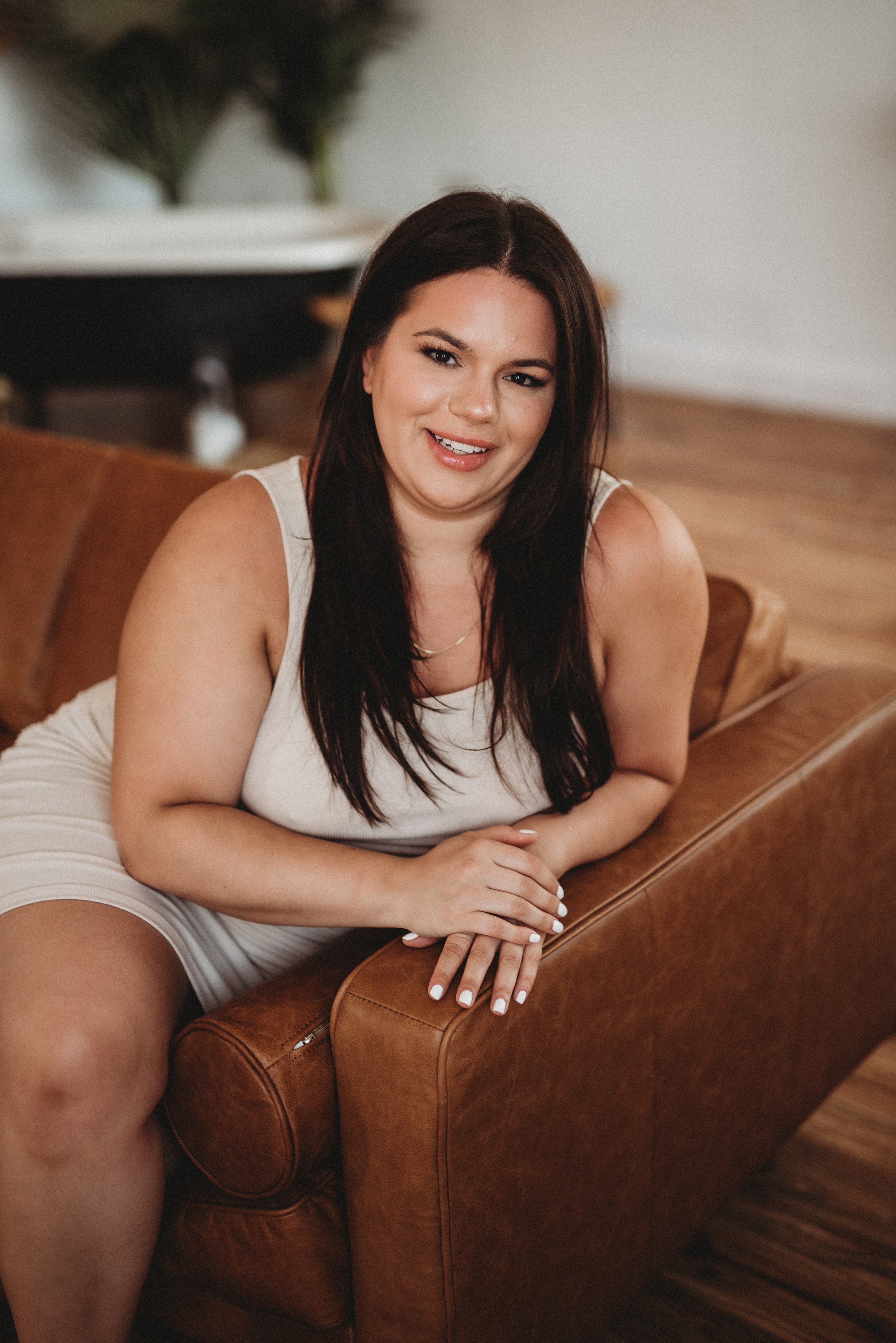 Woman sitting on a brown leather couch, smiling, indoor setting.