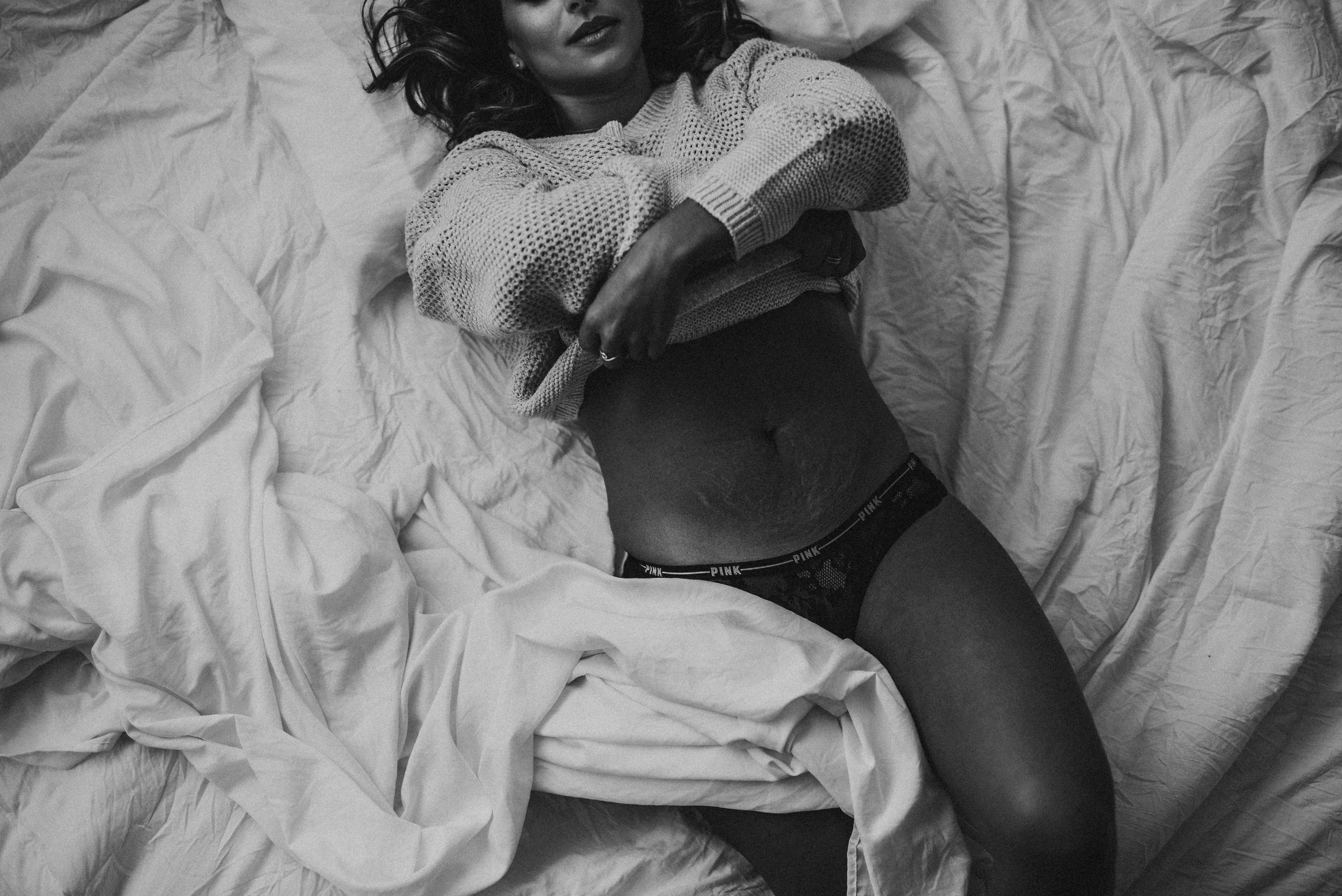 Woman lying on bed wearing a sweater and underwear, with sheets around her.