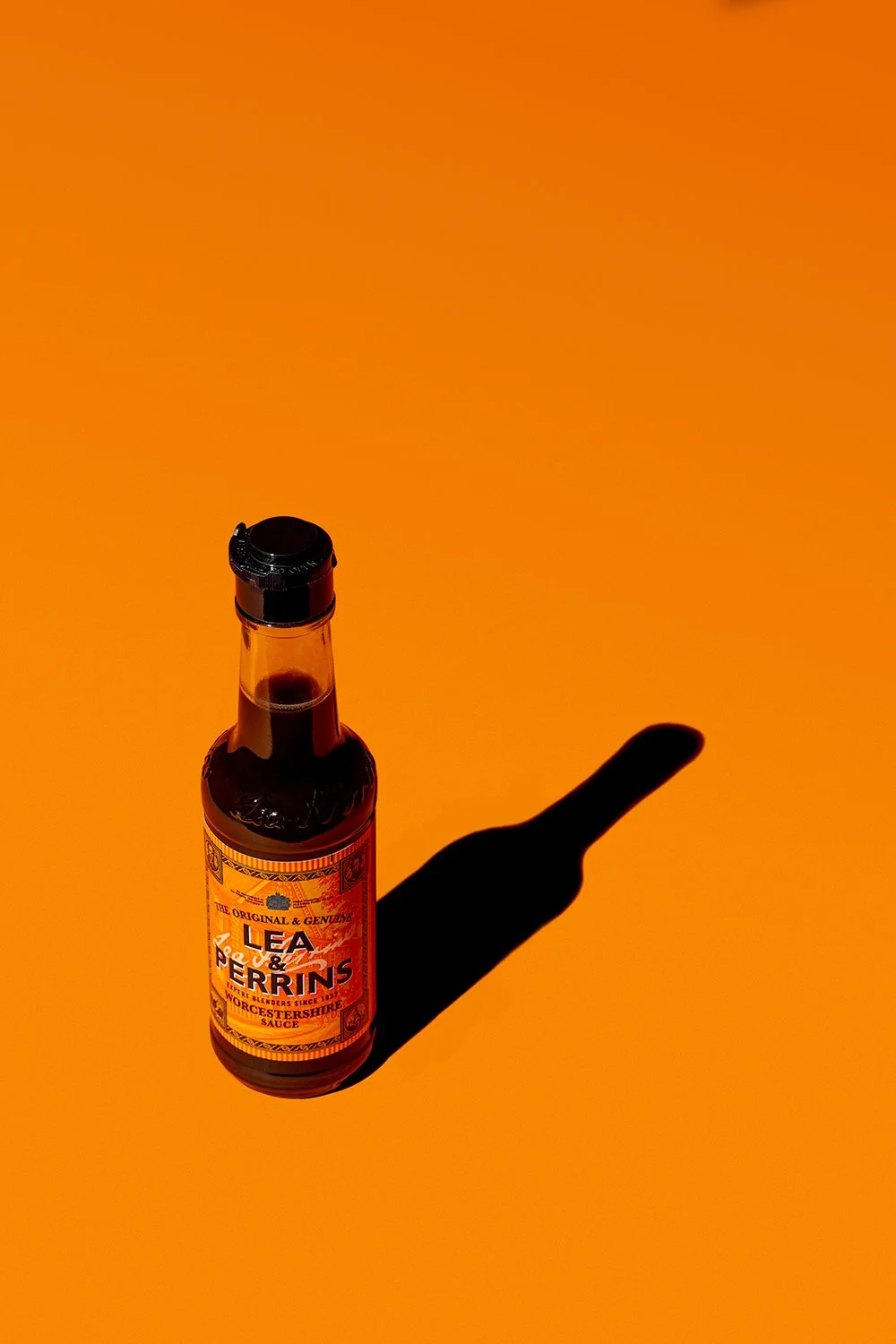 Lea & Perrins bottle of Worcestershire sauce on bright orange background with a long dark crisp shadow professional sauce photography