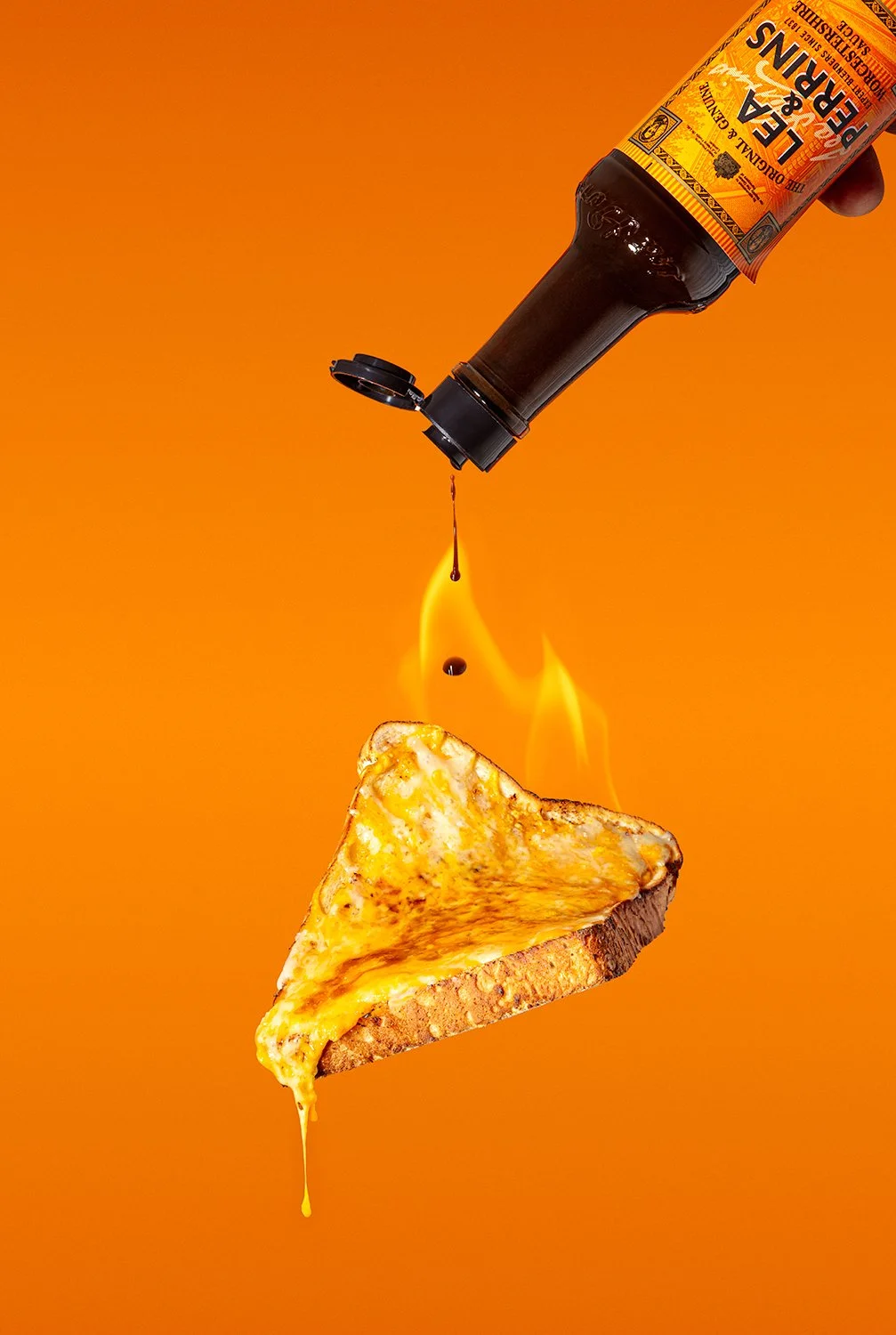 Lea & Perrins Worcestershire sauce dripping onto melted cheese on toast floating in air with fire and bright orange background professional sauce photography