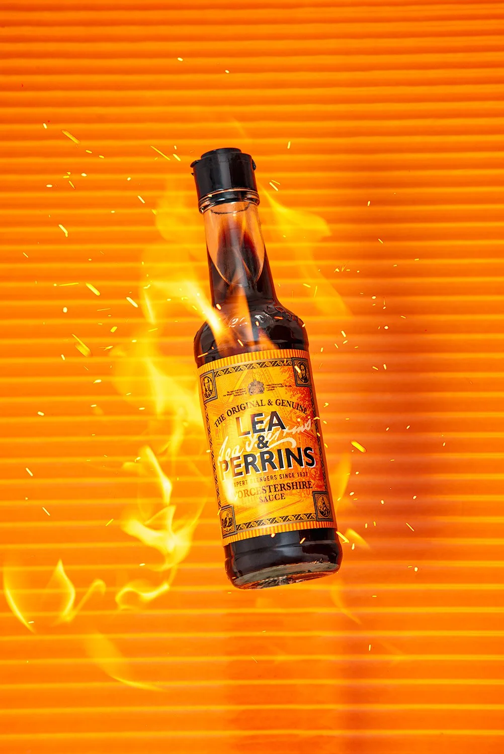 Lea & Perrins Worcestershire sauce bottle with fire and sparks on a striped bright orange background professional sauce photography