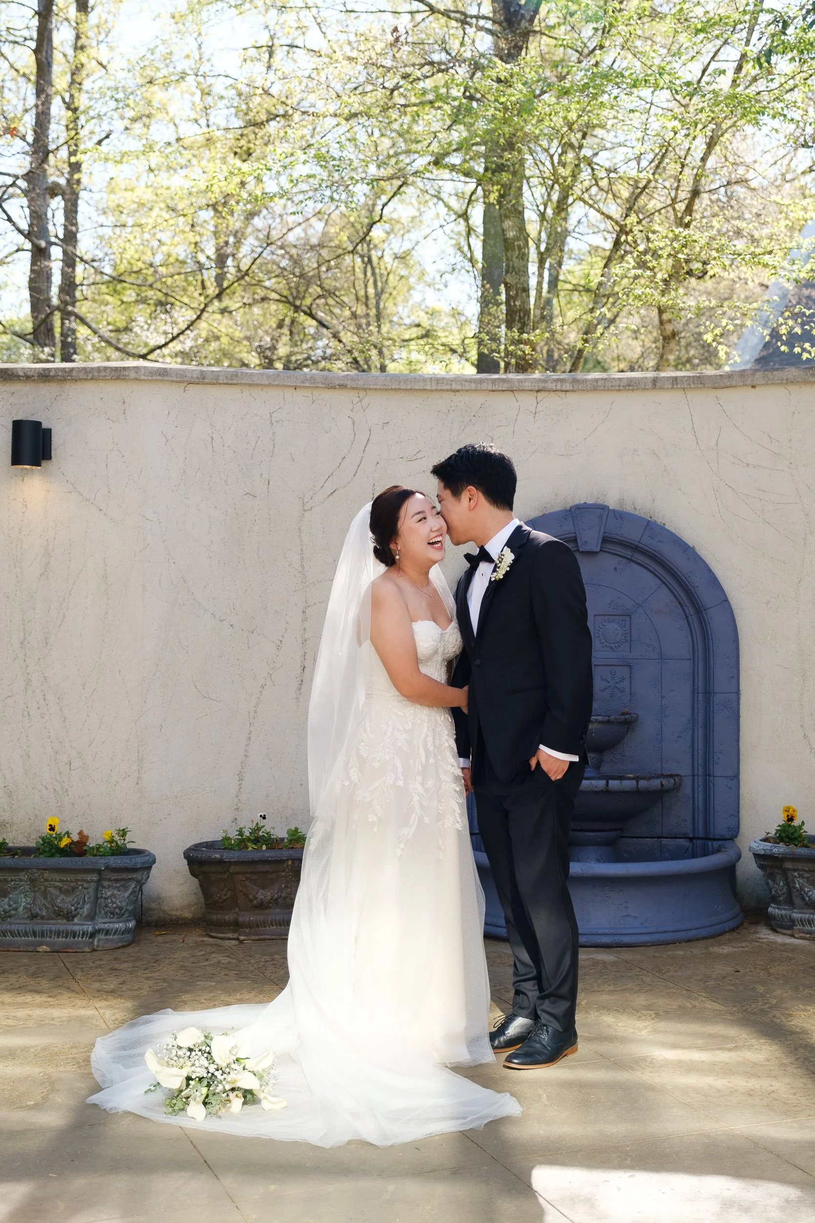 Angella and Austin share a laugh beside a stone fountain at Ashton Gardens North, a Houston wedding venue