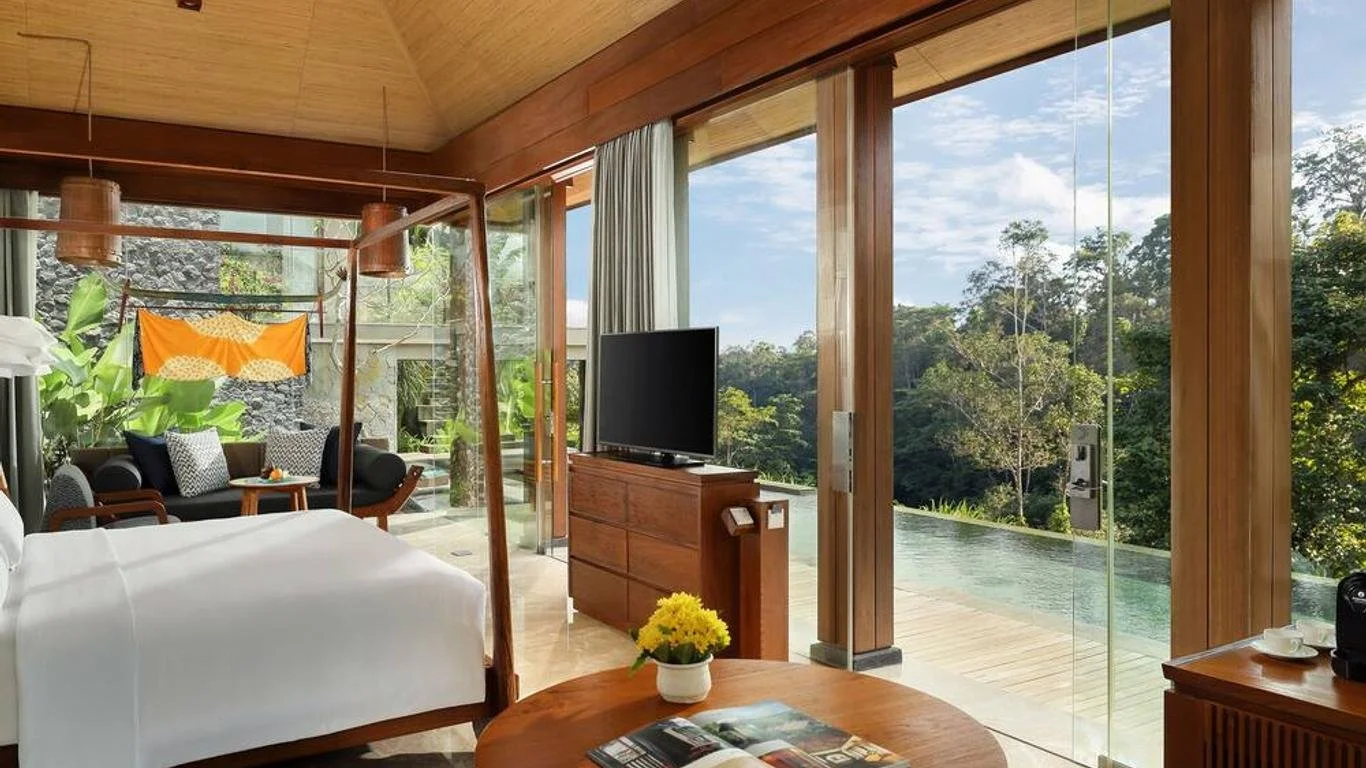 Luxury hotel room with large windows, wooden interior, bed, TV, pool view, and forest backdrop.