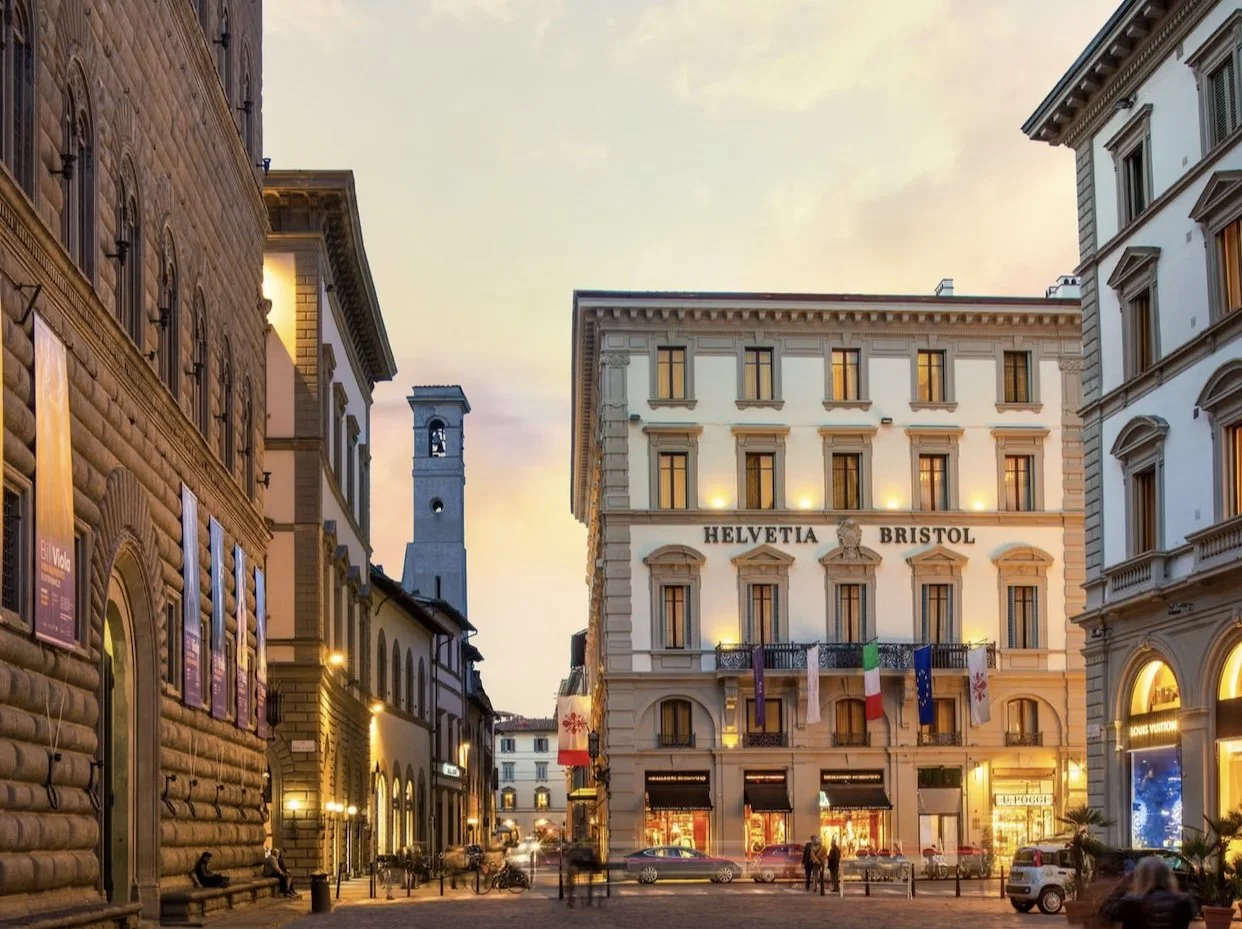 Street view of Helvetia Bristol Hotel in Florence during sunset, with stone building facades, a bell tower, and pedestrians.