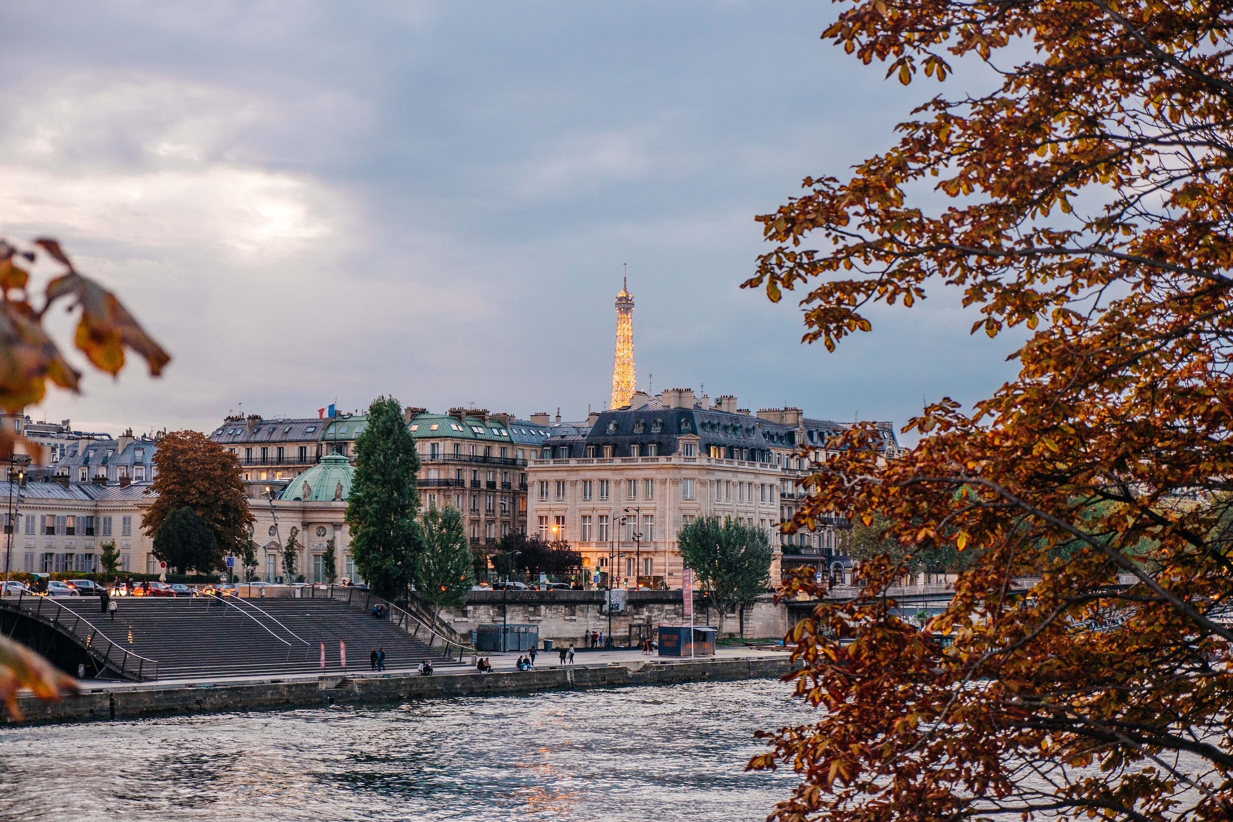 View of Eiffel Tower and Paris cityscape at dusk with autumn leaves and Seine River.