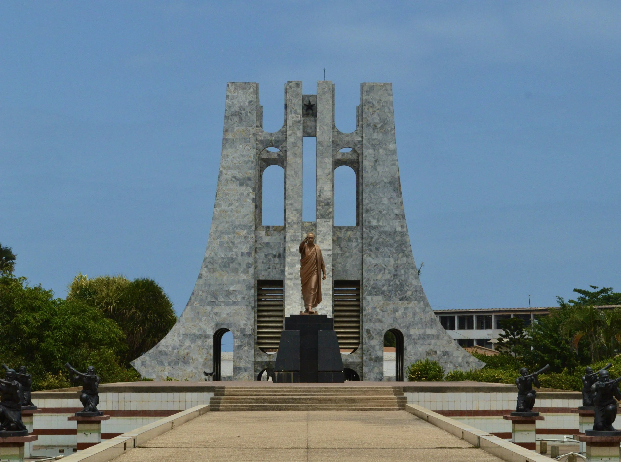 Kwame Nkrumah Mausoleum in Accra, Ghana, featuring a statue of a man in front of a distinctive curved stone structure against a blue sky.