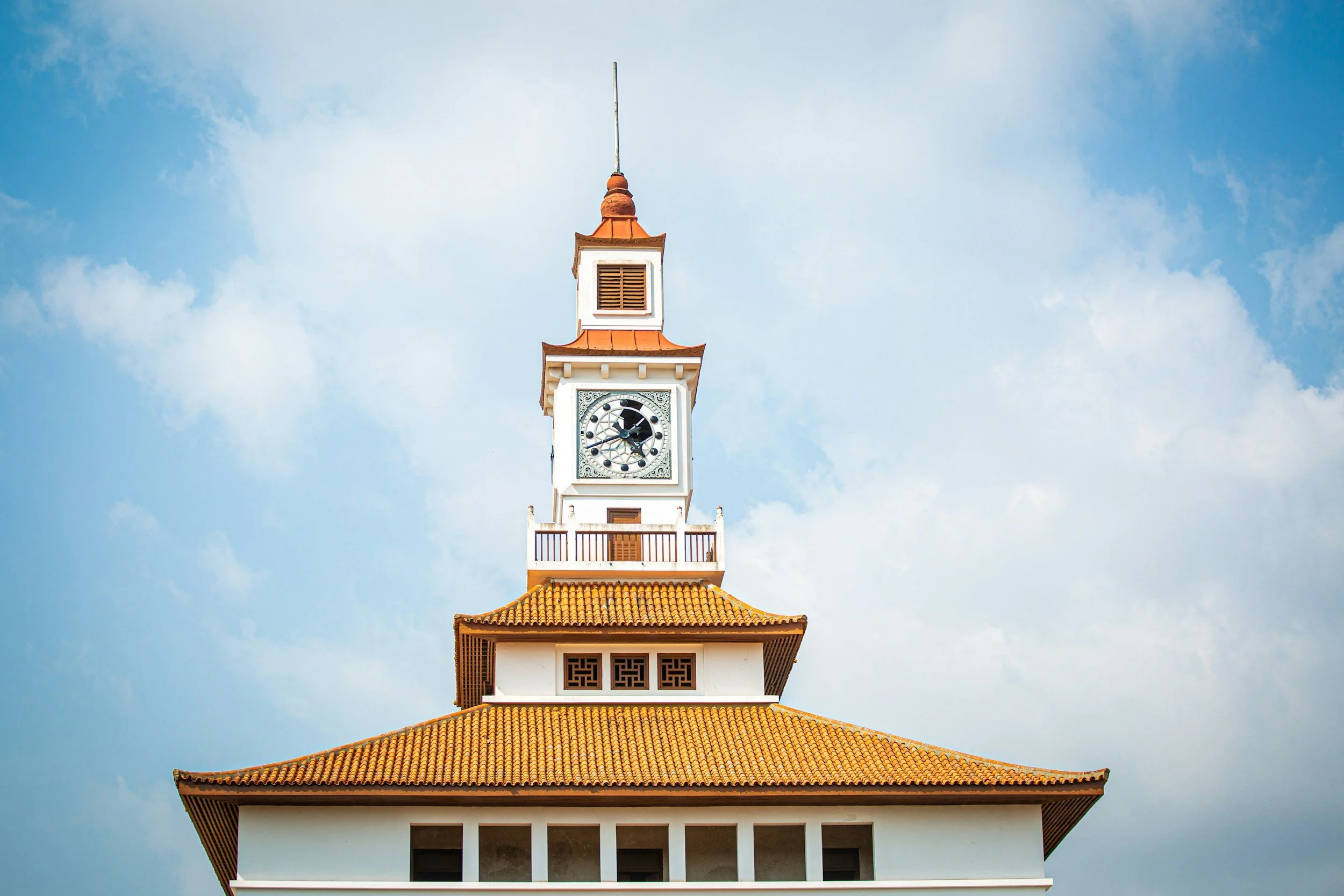 Clock tower with red-tiled roof against blue sky.