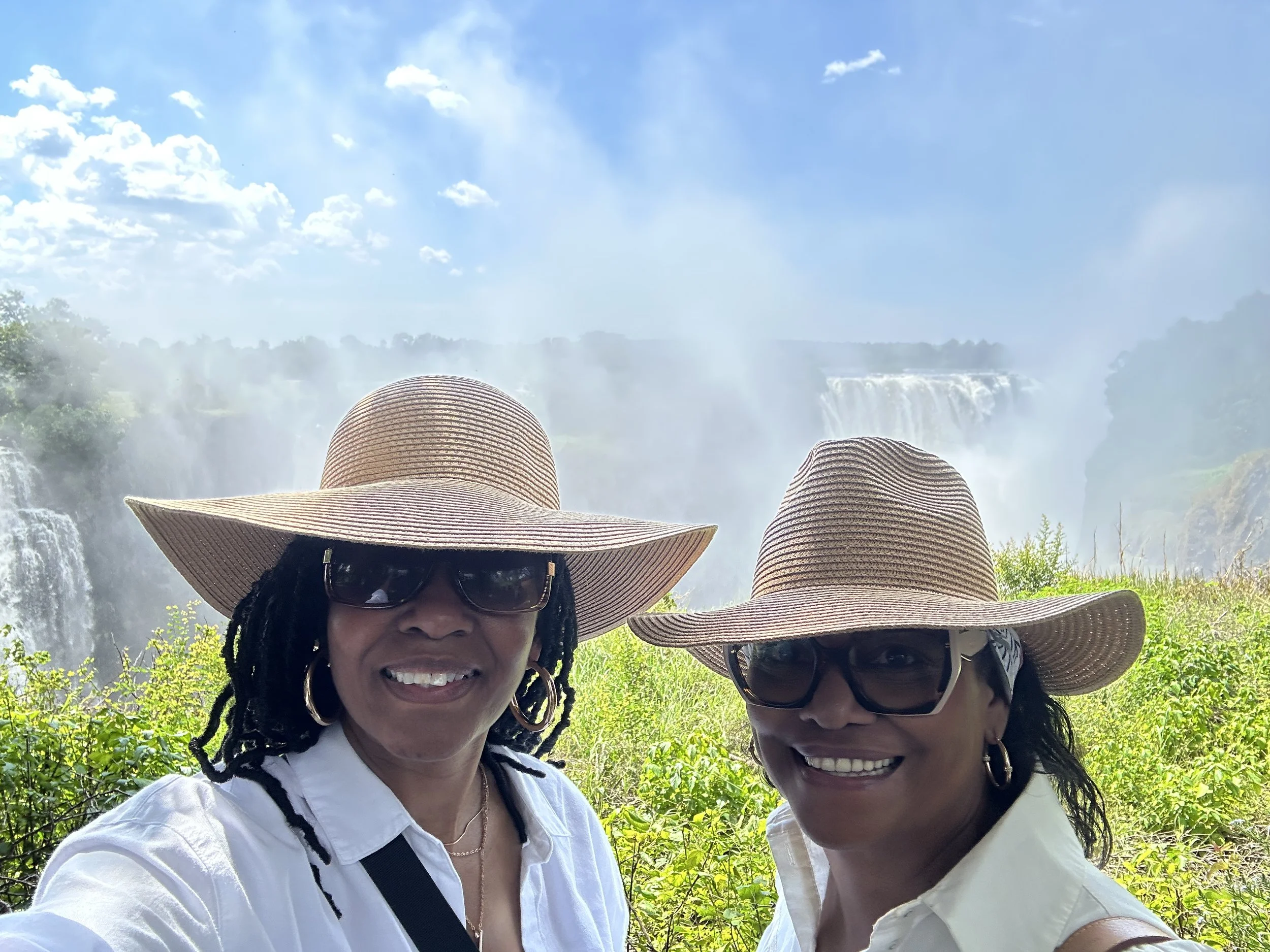 Woman in a straw hat takes a selfie in front of a colorful mural with portraits and the words 'Kutura ri Palenge sendá Galipotana.'