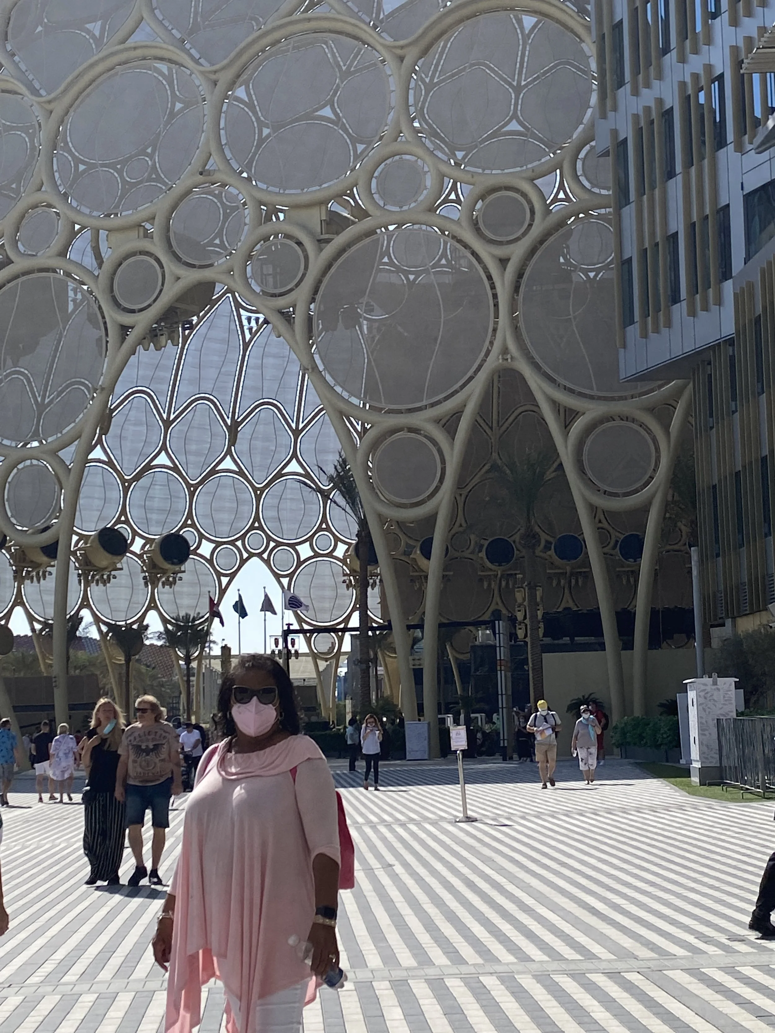 People walking outside near a modern building with a distinctive honeycomb-like architectural structure geometric design.