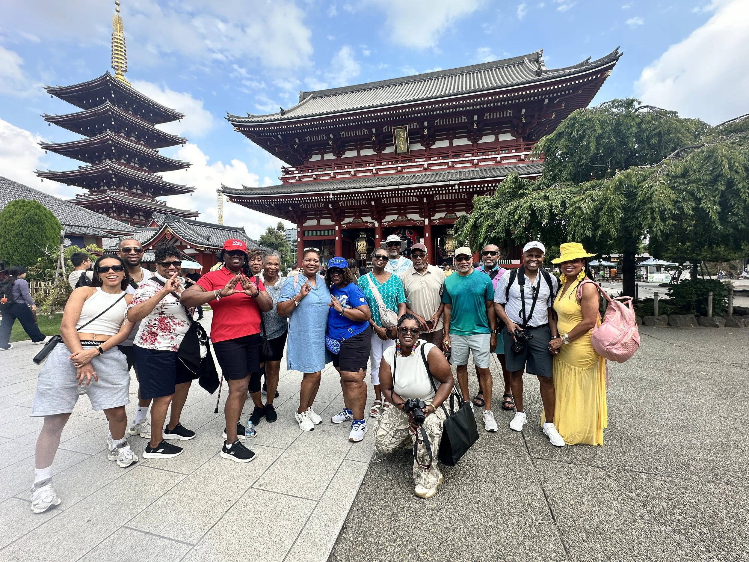 Group of tourists in front of a traditional Japanese temple with a pagoda, during a sunny day.